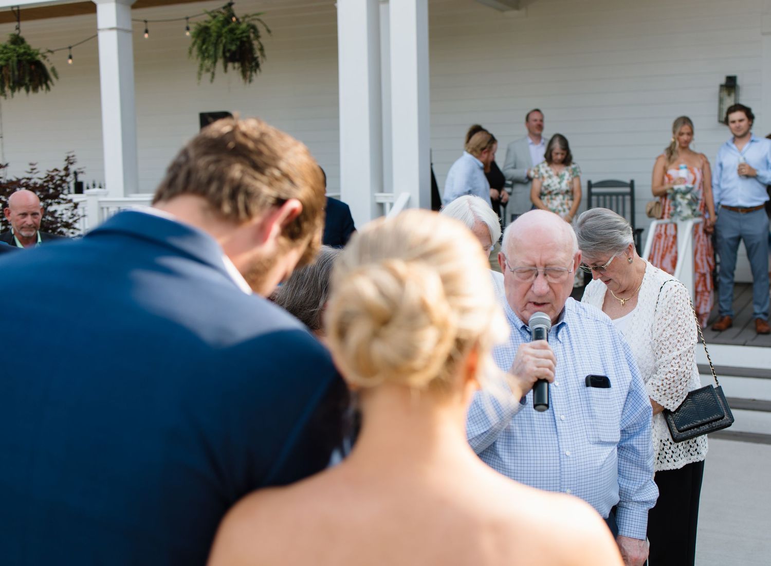 Wedding guests gather on a white porch for an outdoor celebration during a summer afternoon.