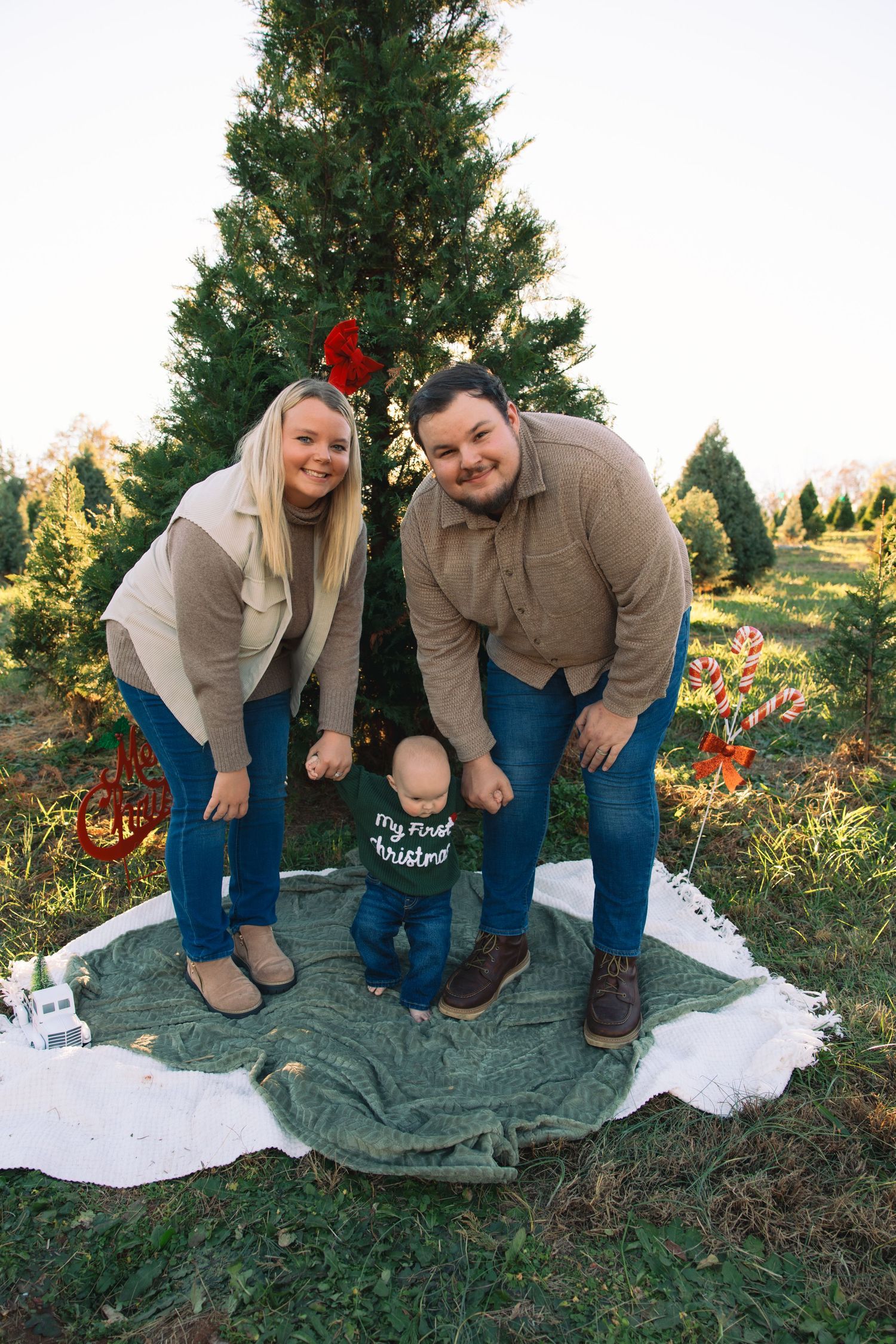 A couple poses together in front of Christmas trees at a tree farm during golden hour sunset.