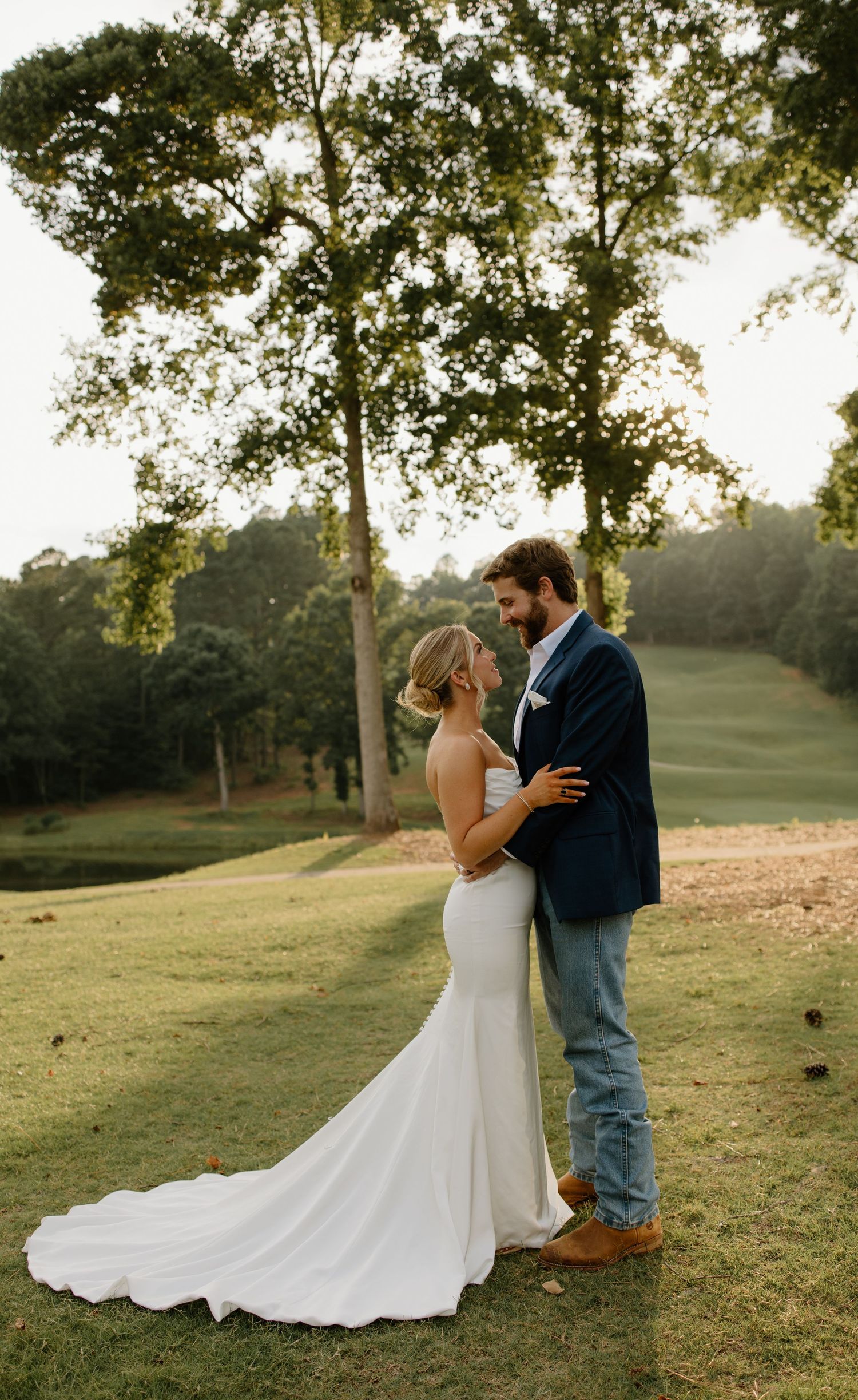 A couple shares romantic moments in a grassy field during golden hour, with the bride wearing a flowing white wedding dress.