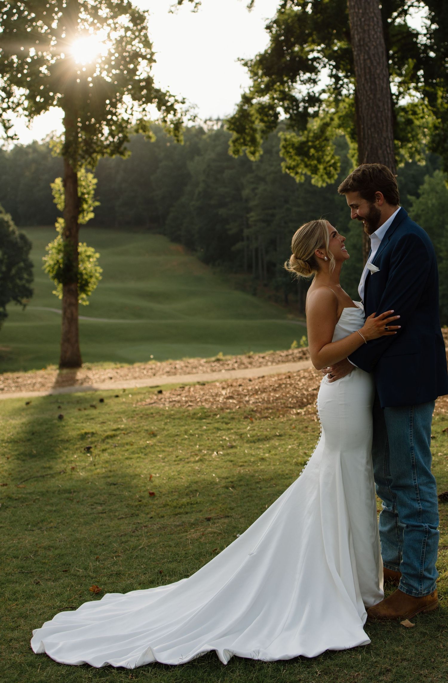 Couple embraces on a hilltop golf course during golden hour sunset.