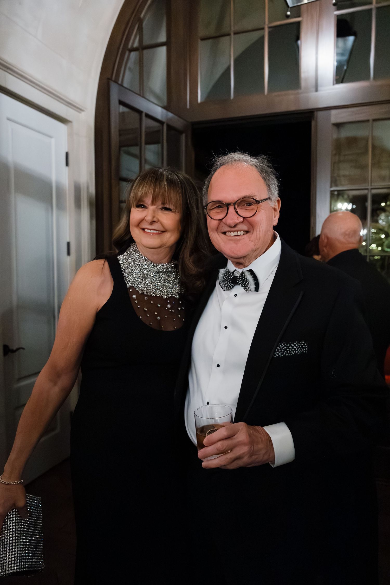 Elegantly dressed couples enjoying a formal evening event in a brightly lit hallway.