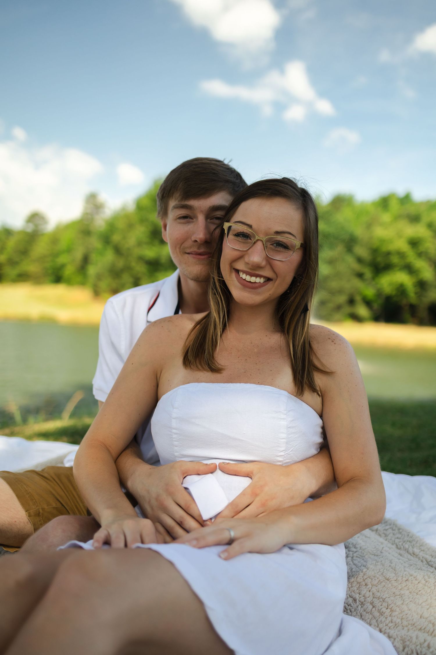 Expectant couple sharing intimate moment while holding ultrasound images on picnic blanket.