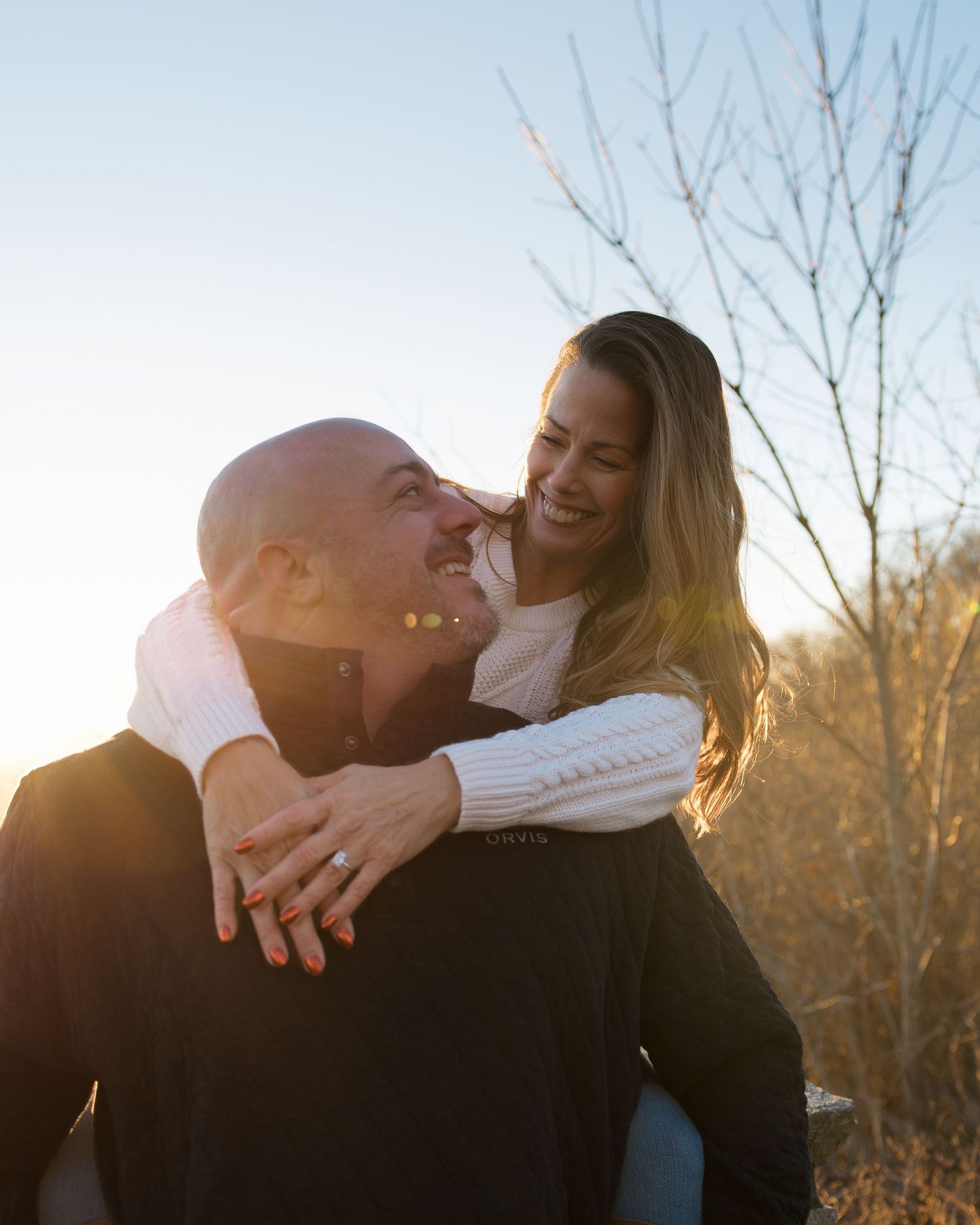 A romantic sunset moment captured of a couple embracing outdoors with bare trees in the background.