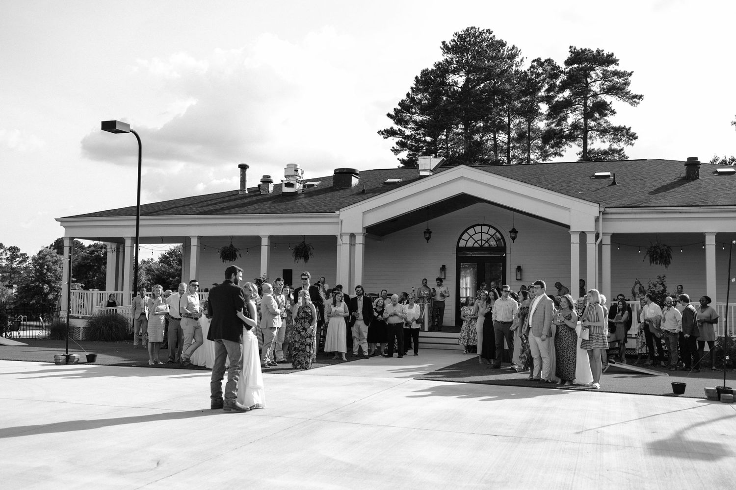 A crowd of people gathered outside a building entrance with pine trees in the background.