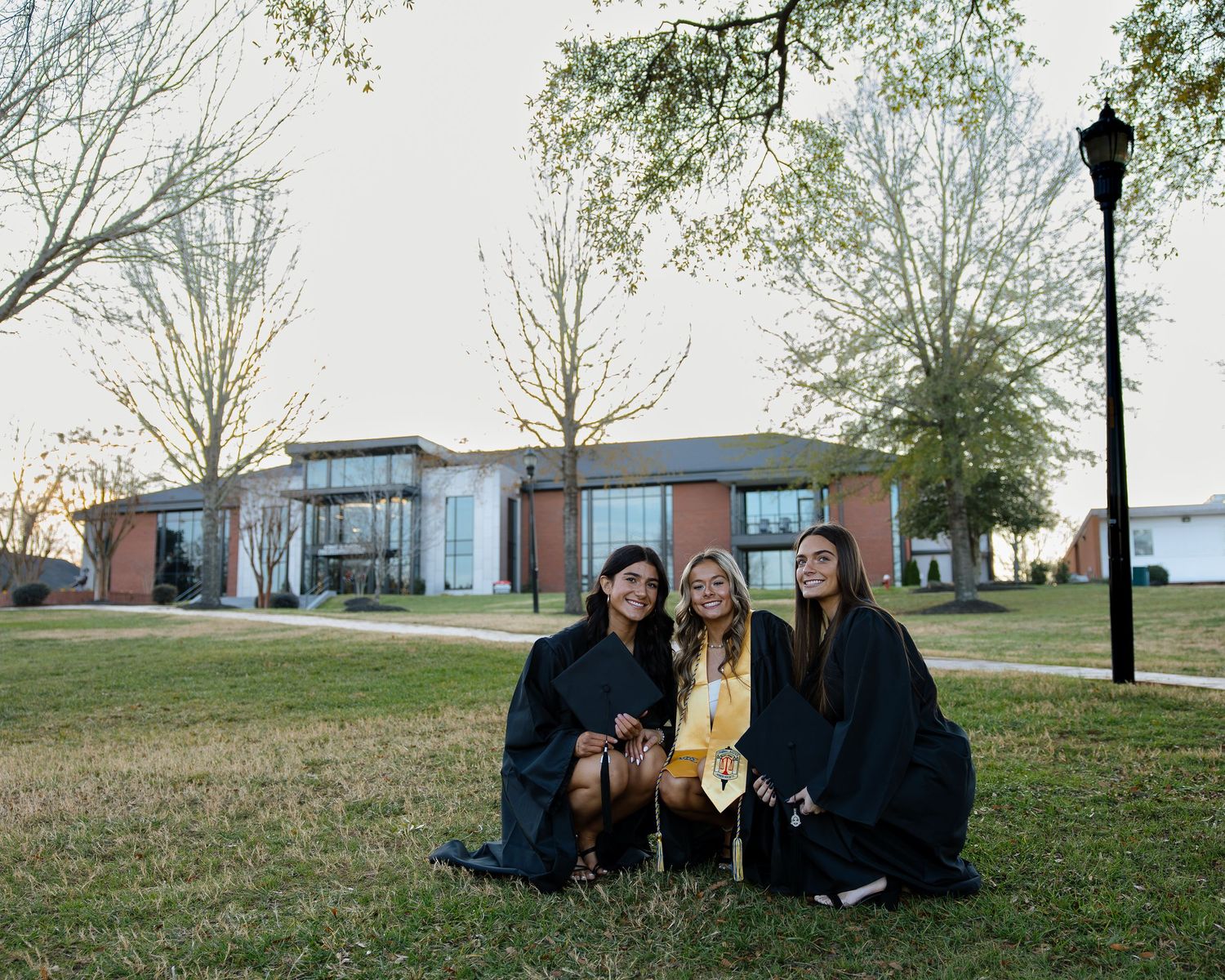 Graduates in black gowns sitting together on grass during outdoor celebration.