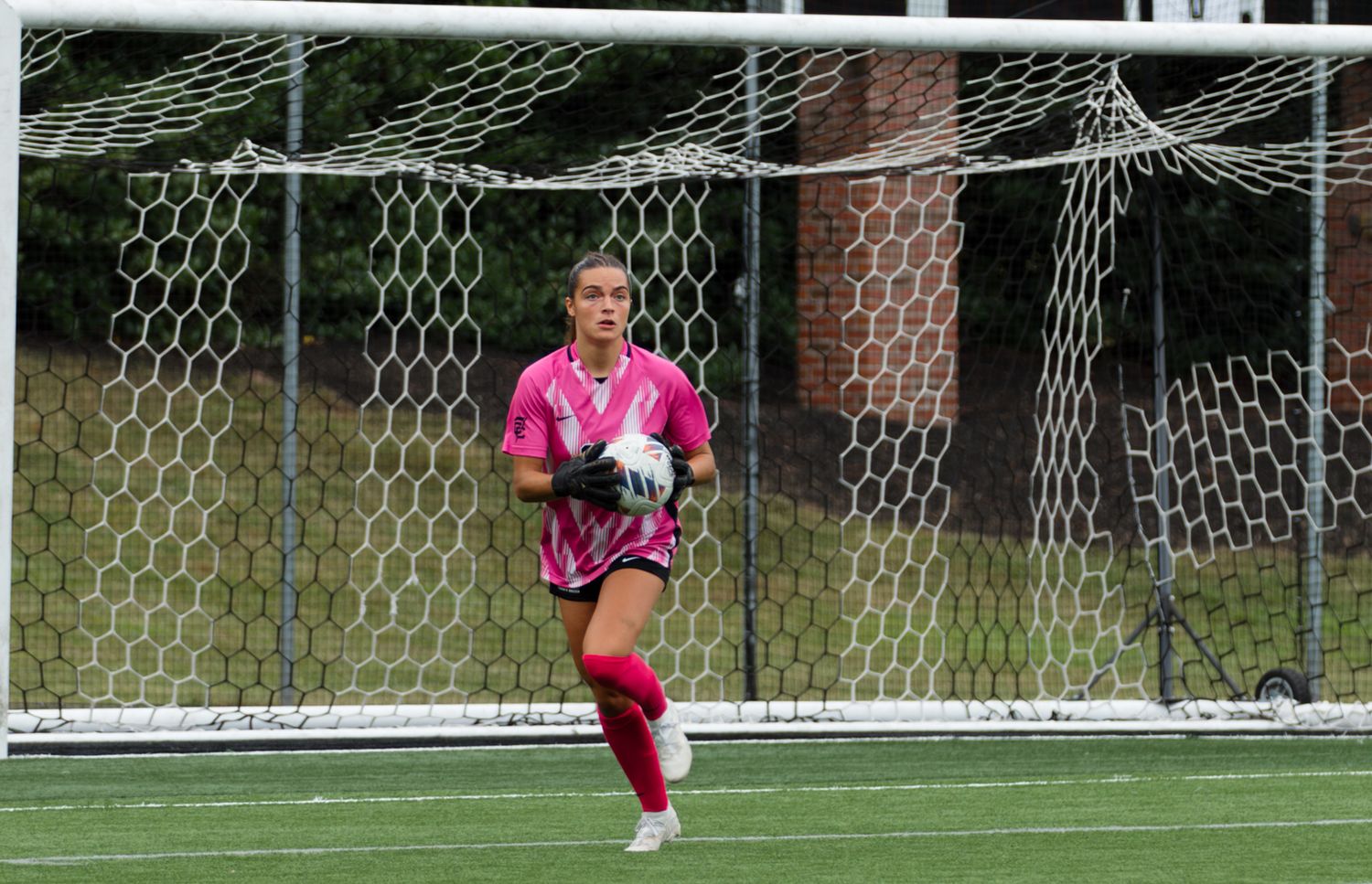 Soccer goalkeeper in pink uniform defending the goal during game