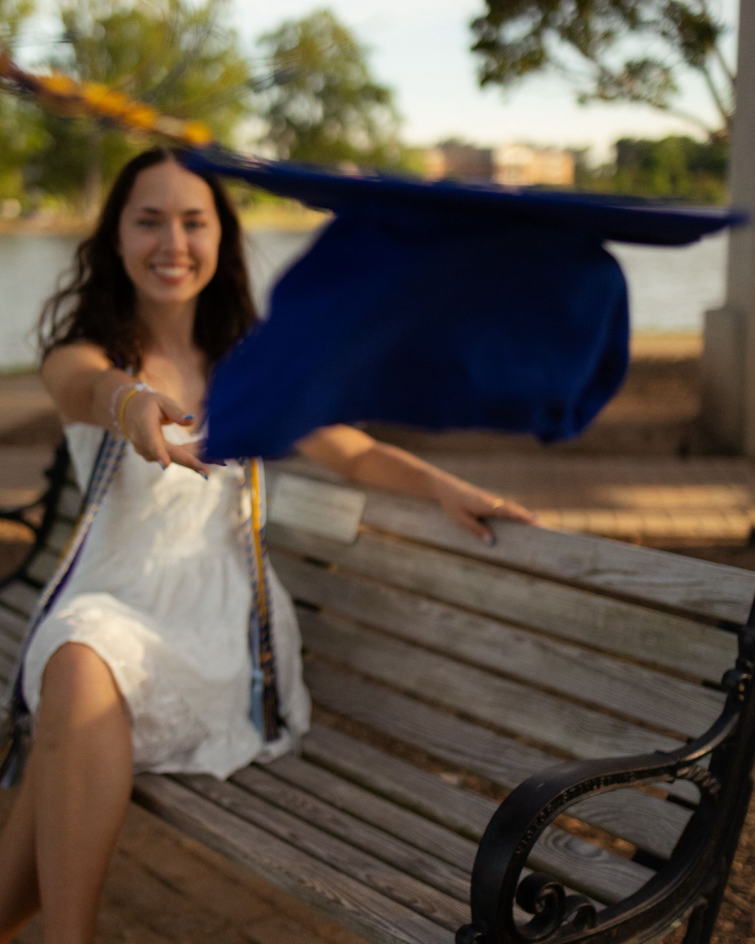 A wooden park bench sits in warm sunlight with graduation cap and gown.