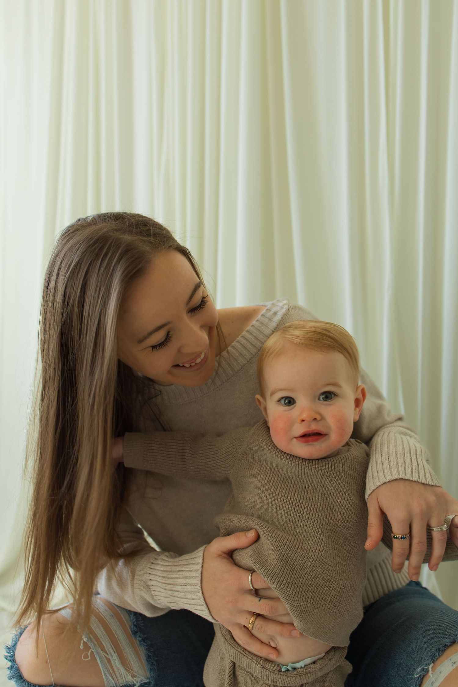 Tender interaction between parent and baby against white curtains.