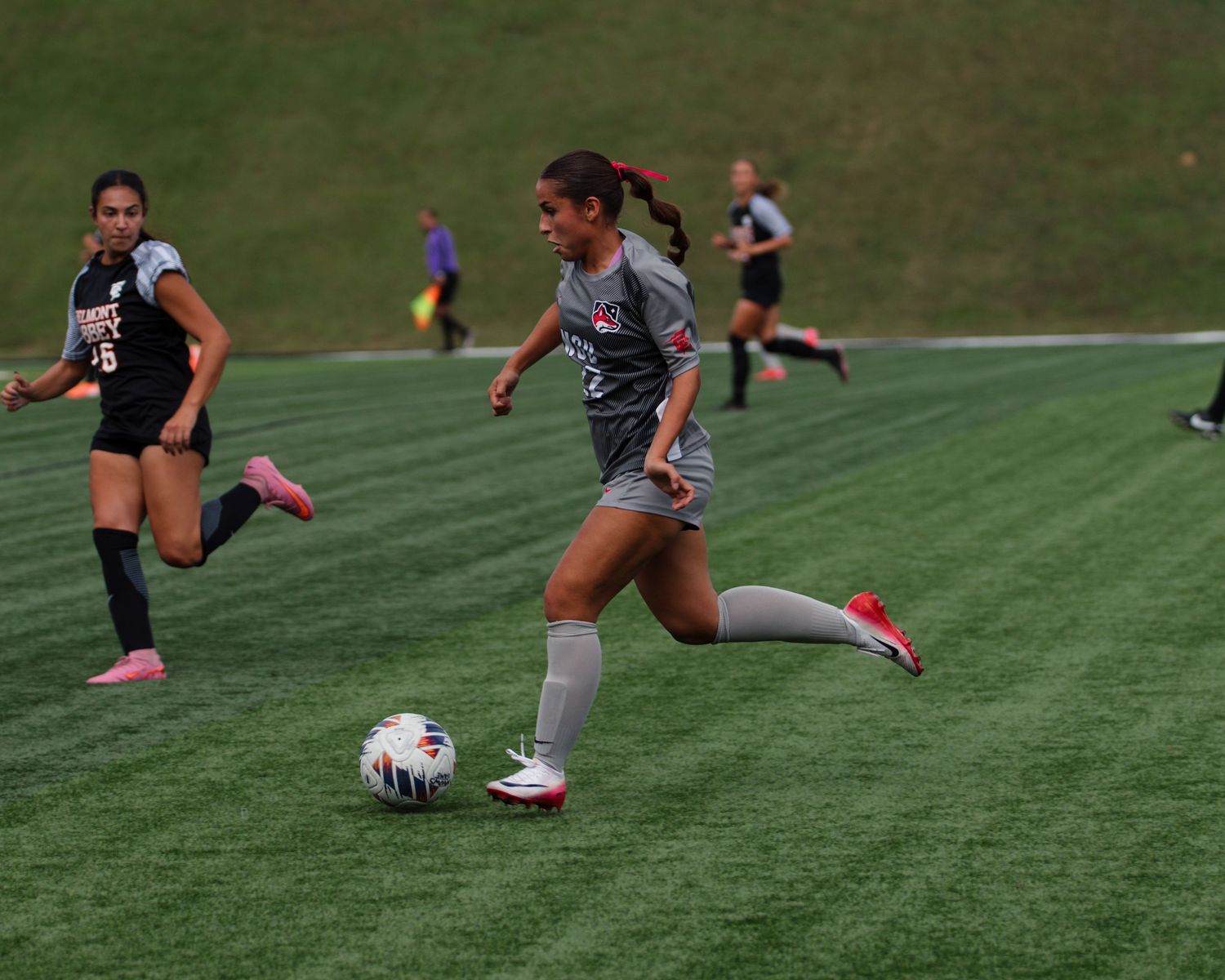 Soccer players running drills with a ball on artificial turf field.