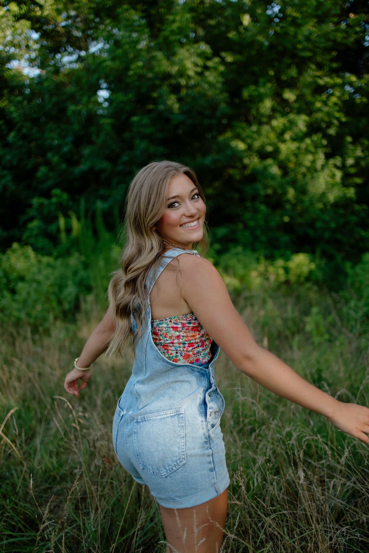 Playful poses in denim overalls against a lush green natural background.