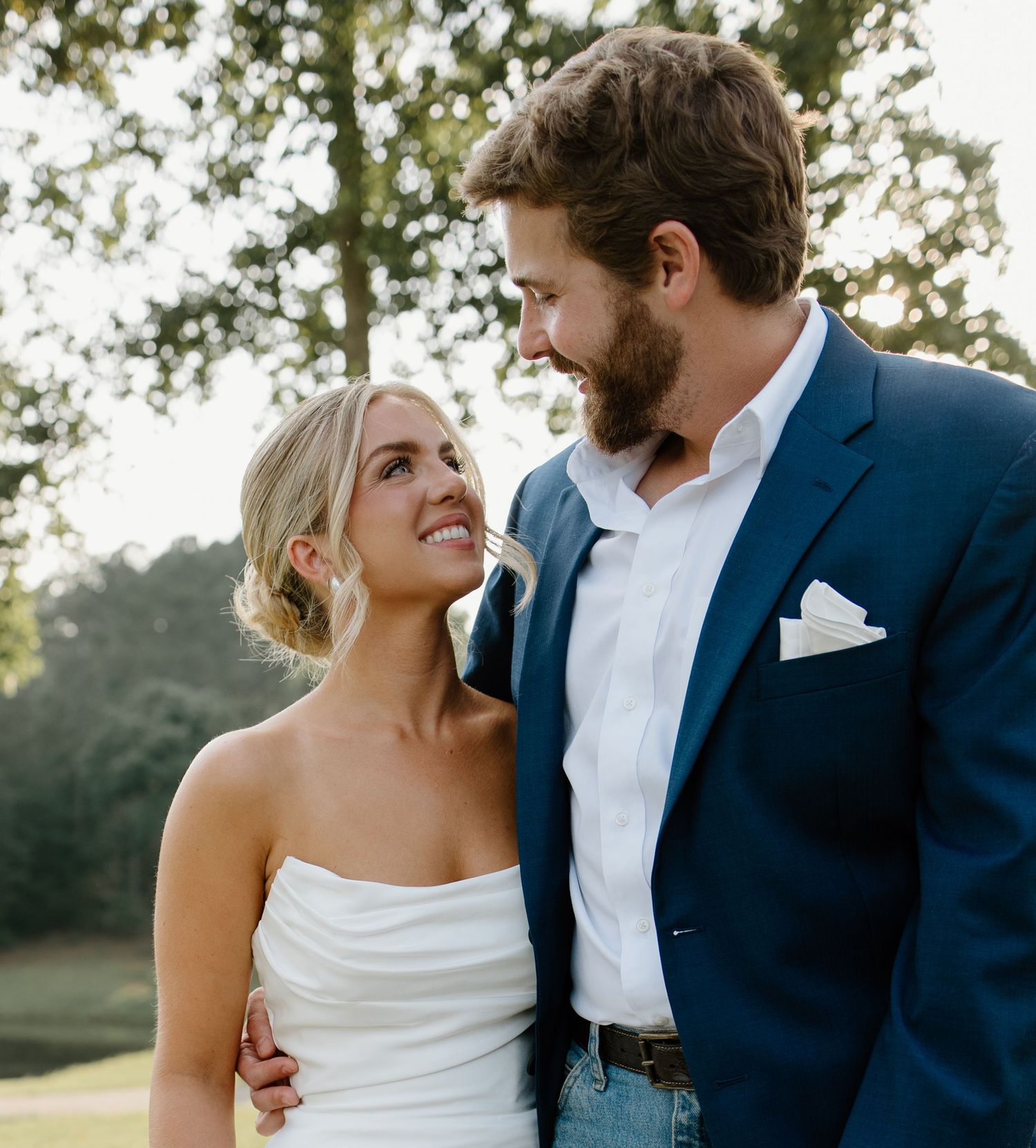 Romantic outdoor couple photoshoot with navy suit and white dress against natural backdrop.