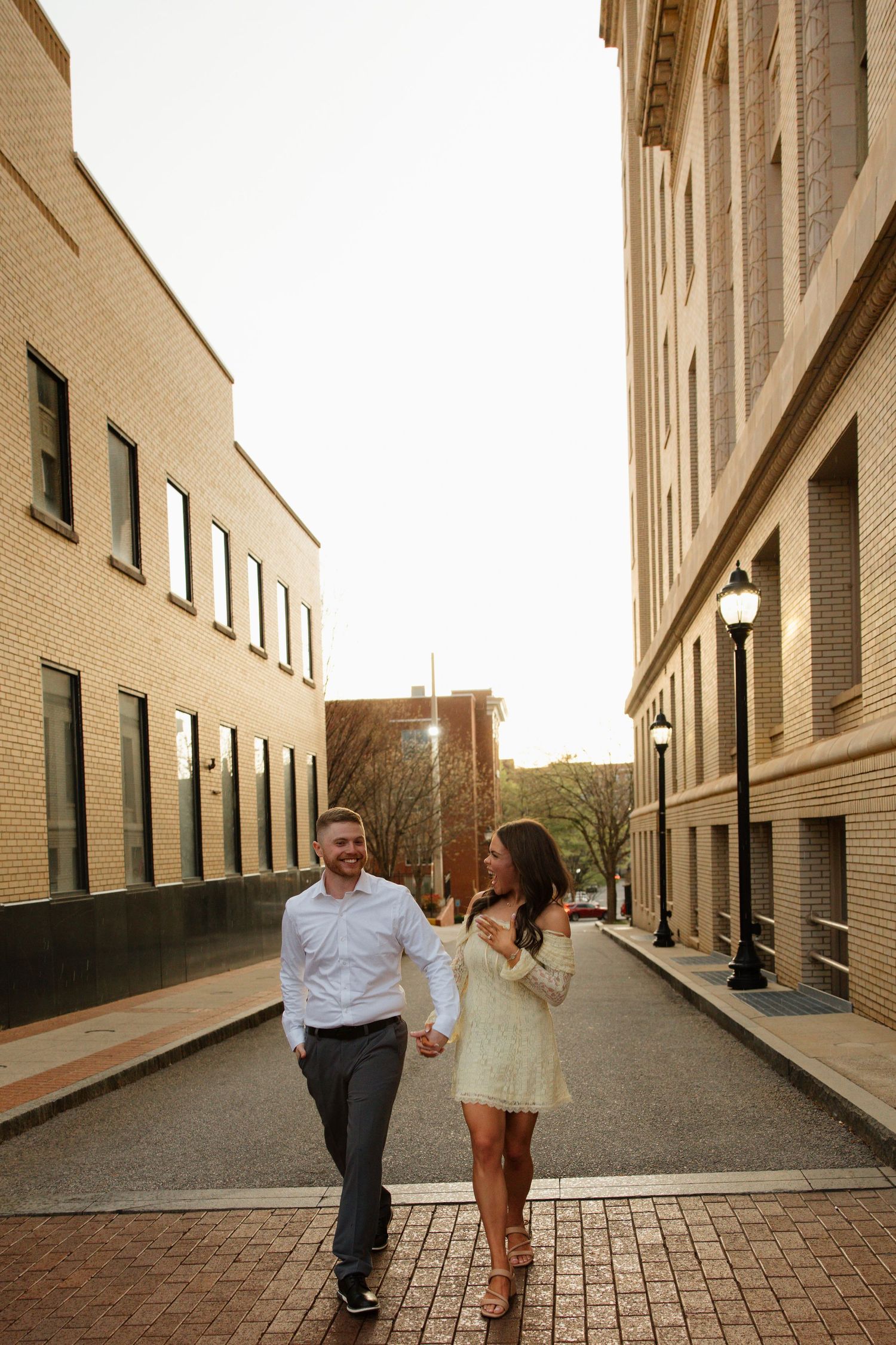 Couple holding hands and walking on a brick alley between buildings during golden hour in an urban setting.