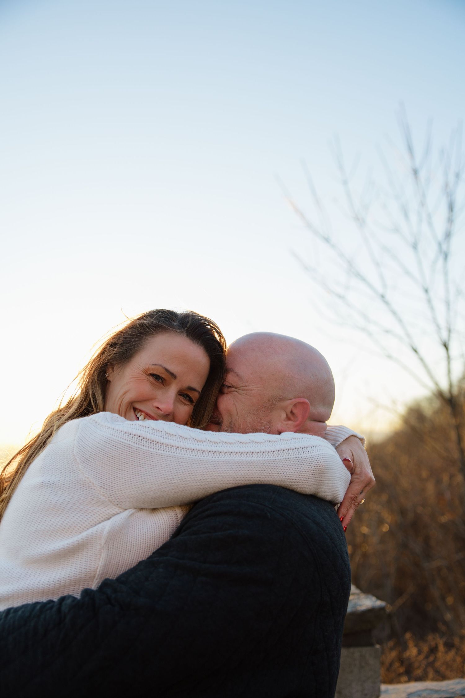 A couple embraces outdoors during golden hour, sharing a joyful moment in cozy winter sweaters.