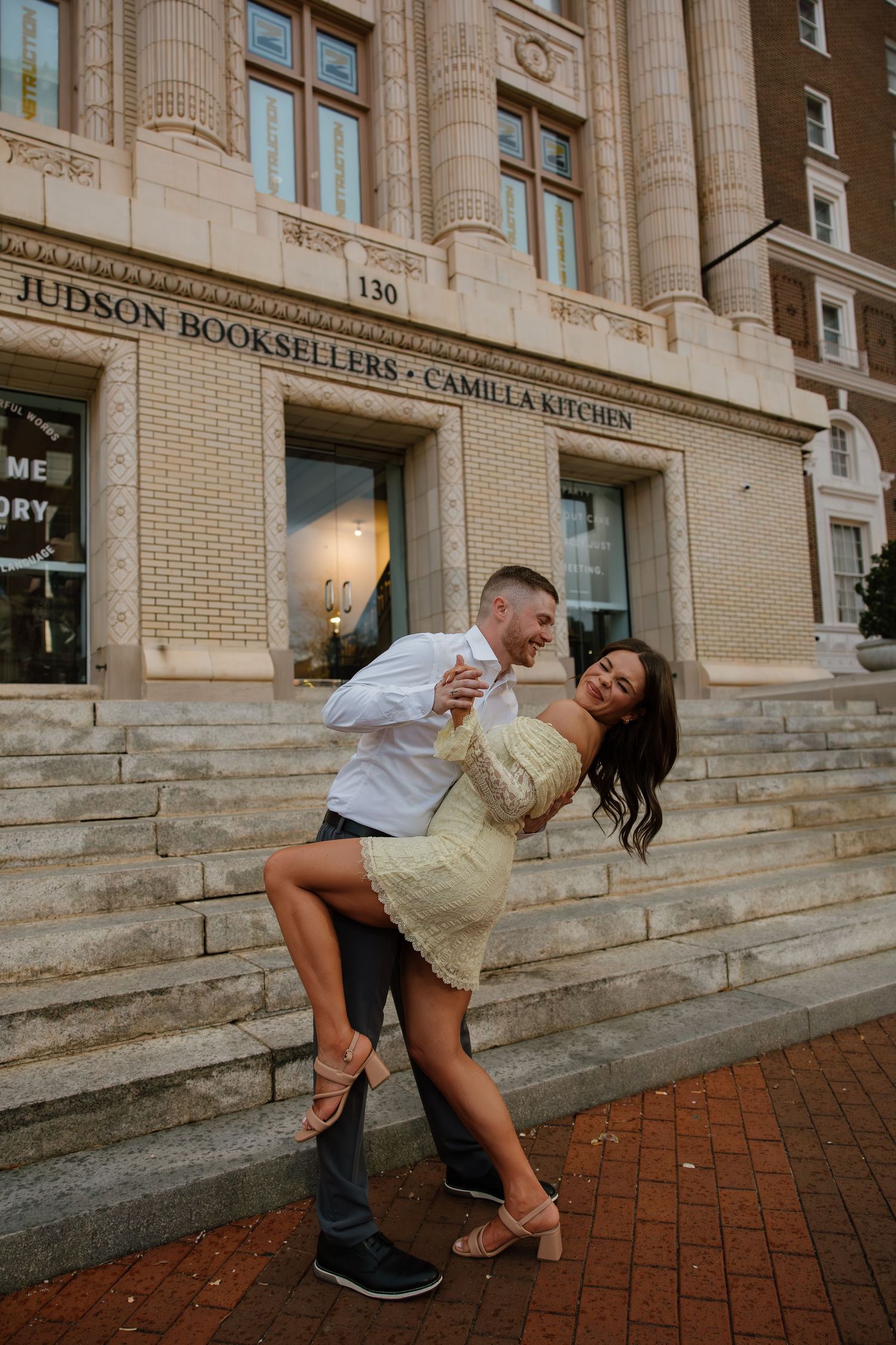 Couple dancing and laughing on steps outside Judson Booksellers and Camilla Kitchen in a romantic engagement photo.