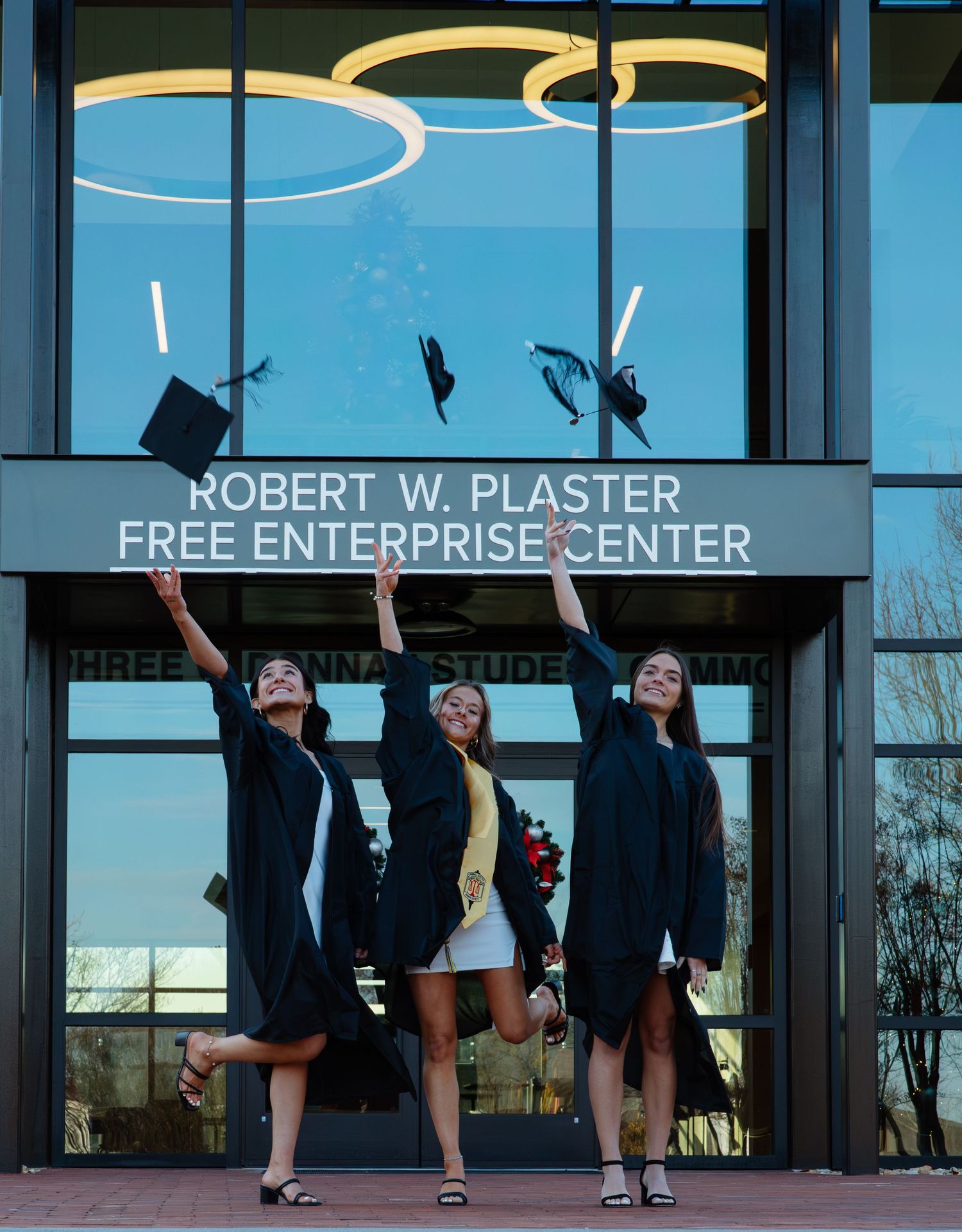 Graduates toss caps in front of the Robert W Plaster Free Enterprise Center.