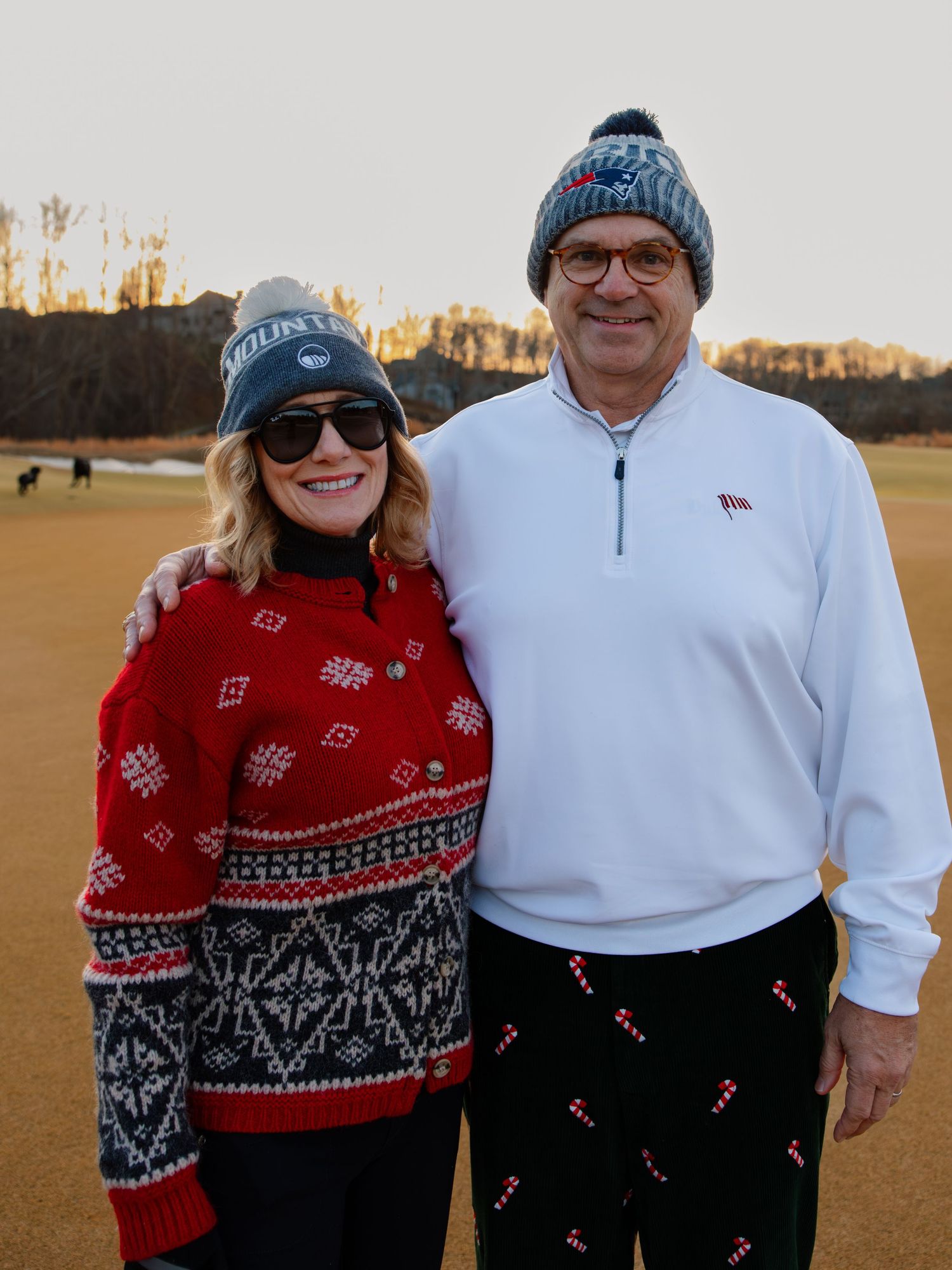 Two people wearing festive winter sweaters pose together outdoors.