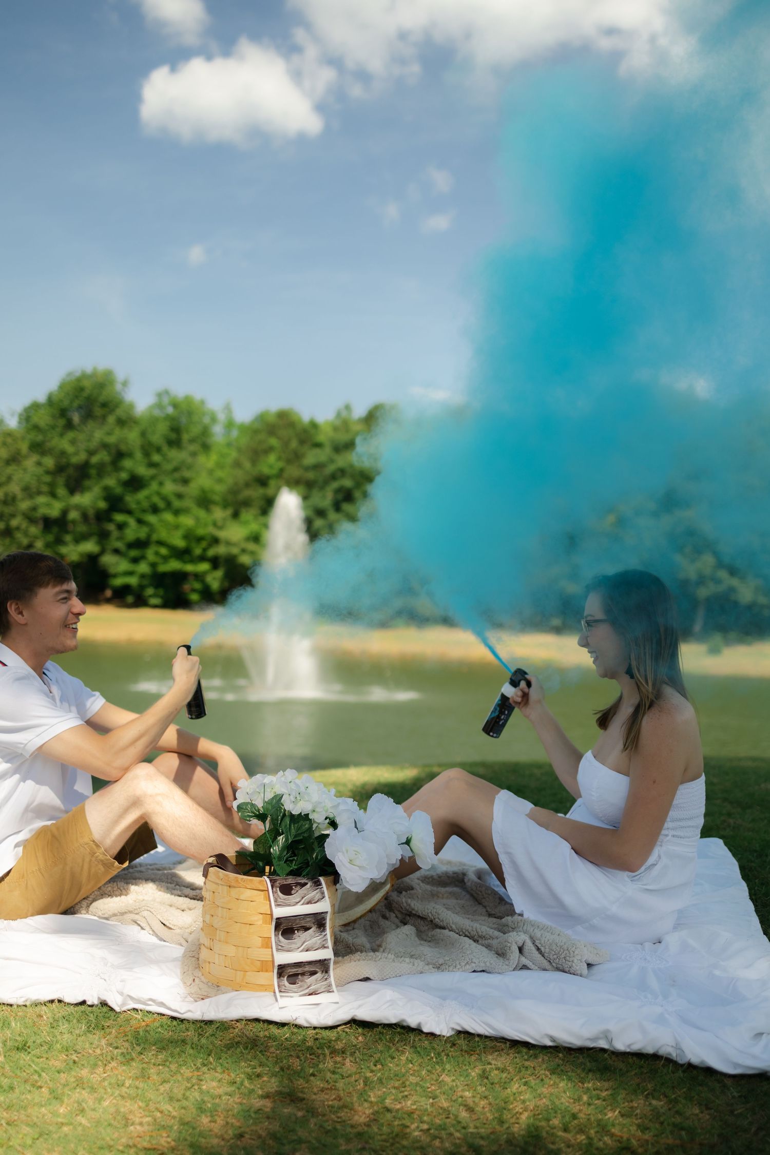 A gender reveal photo sequence showing blue smoke emerging from a smoke bomb on a grassy field with people lying on white fabric.