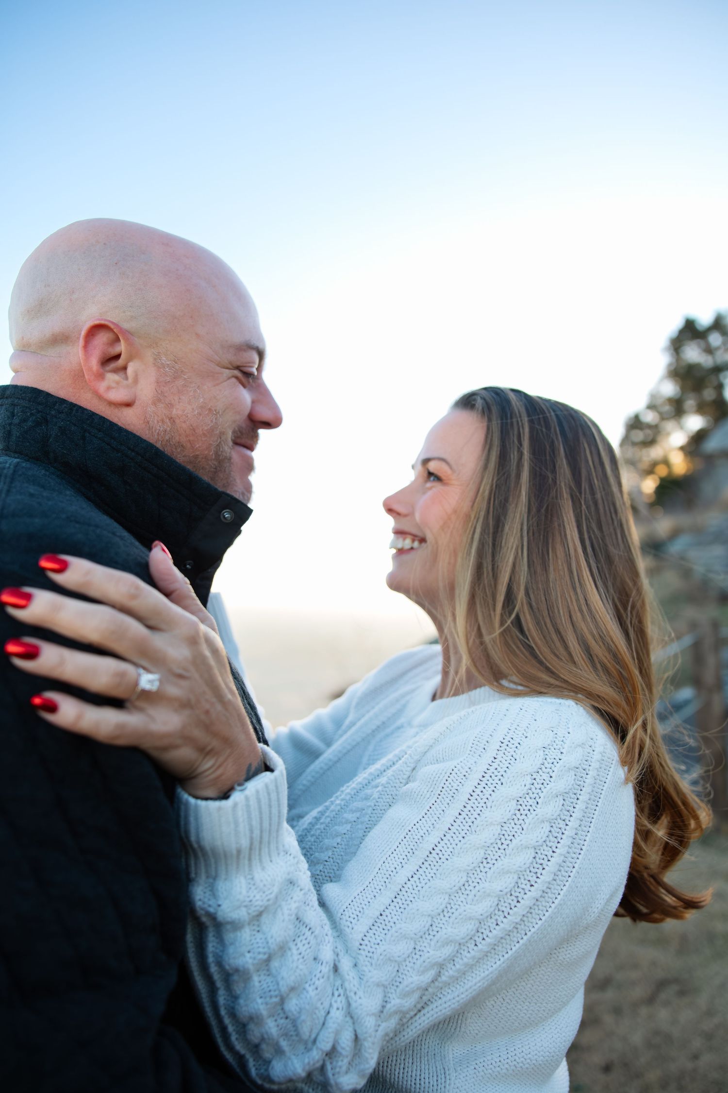 A couple embraces outdoors during sunset wearing a white knit sweater and black coat on a winter day.