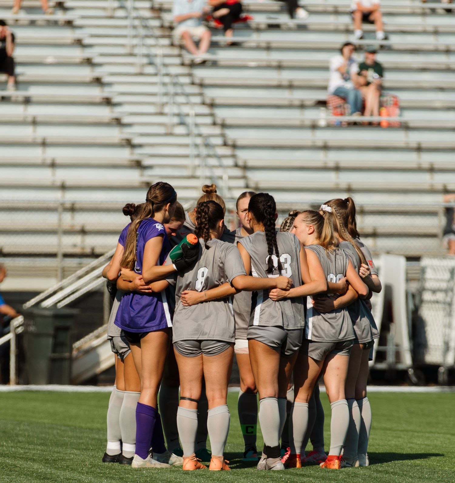 Soccer team huddles together on the field before start of game on sunny day.