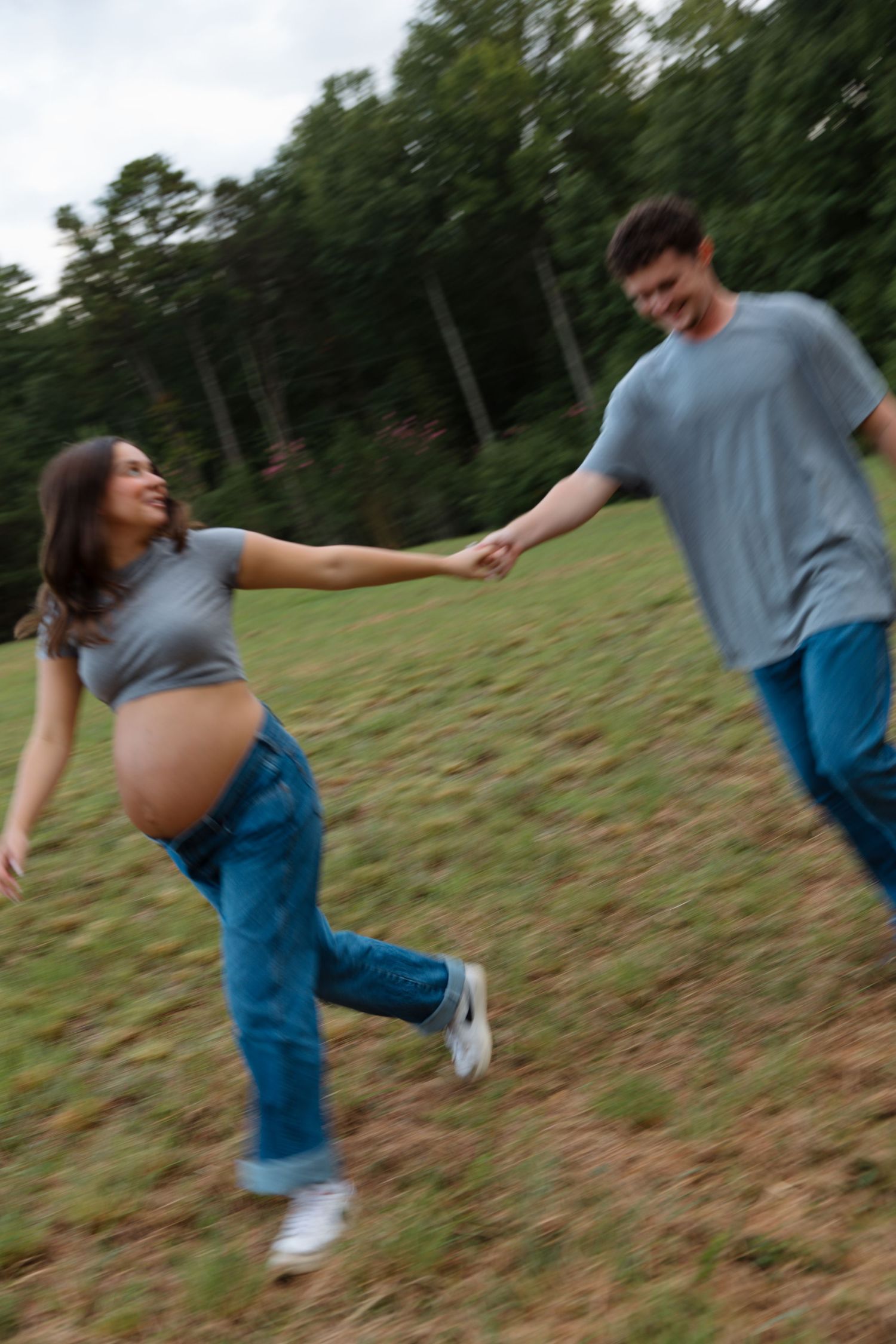 A playful couple dances and spins together on a grassy hillside.