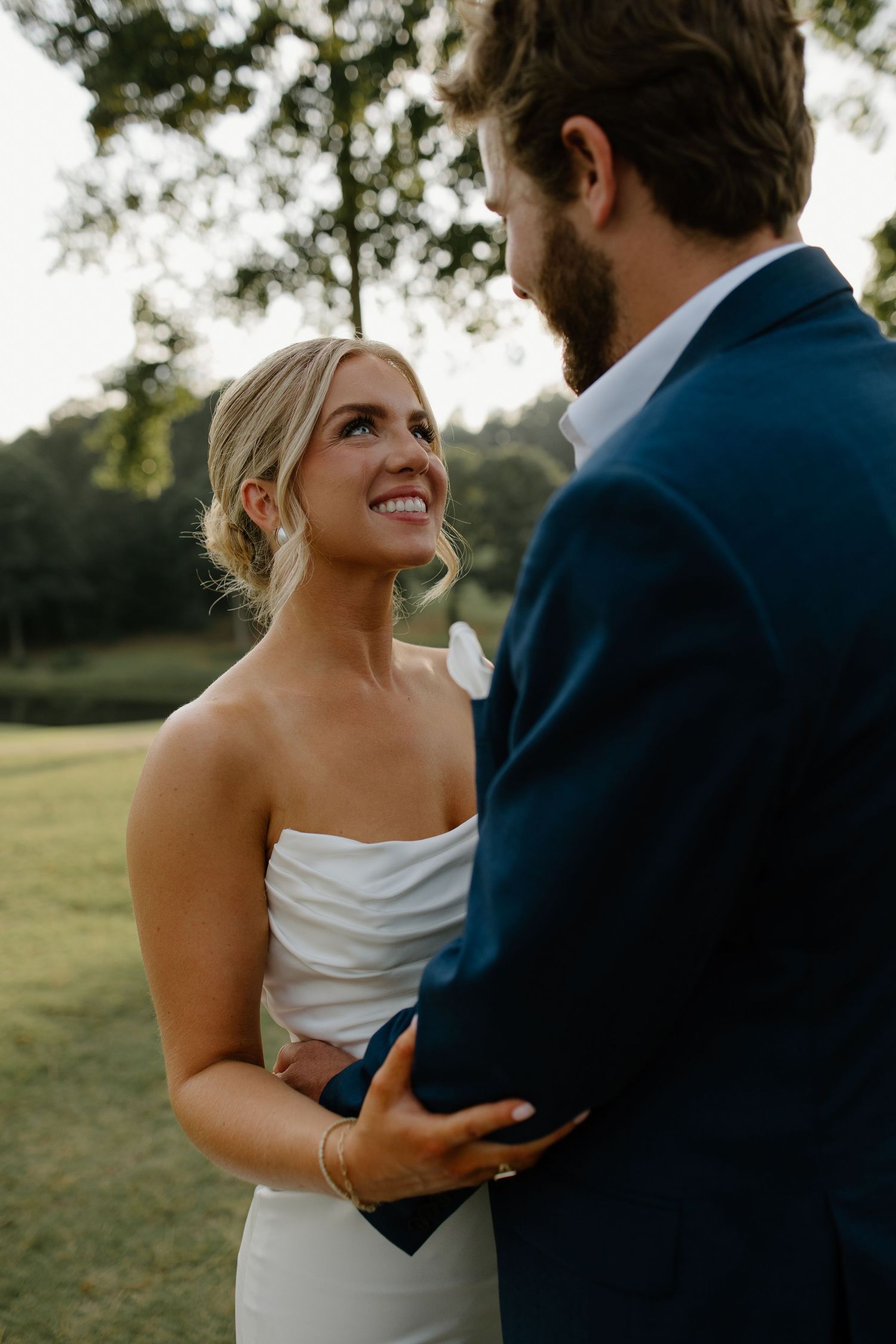 A couple shares an intimate moment outdoors with the bride wearing a white strapless dress and groom in navy suit.