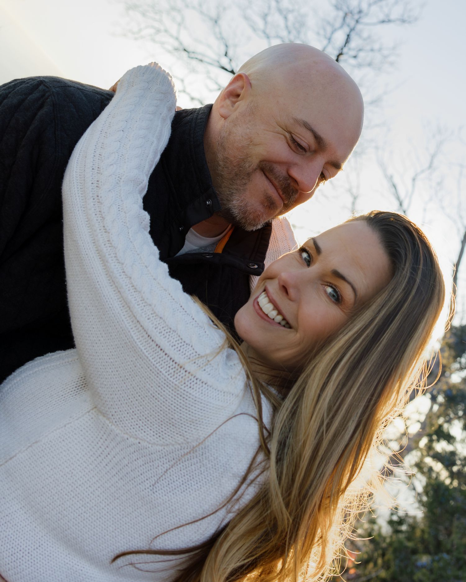 Intimate outdoor portrait of a couple in matching white sweaters at sunset.