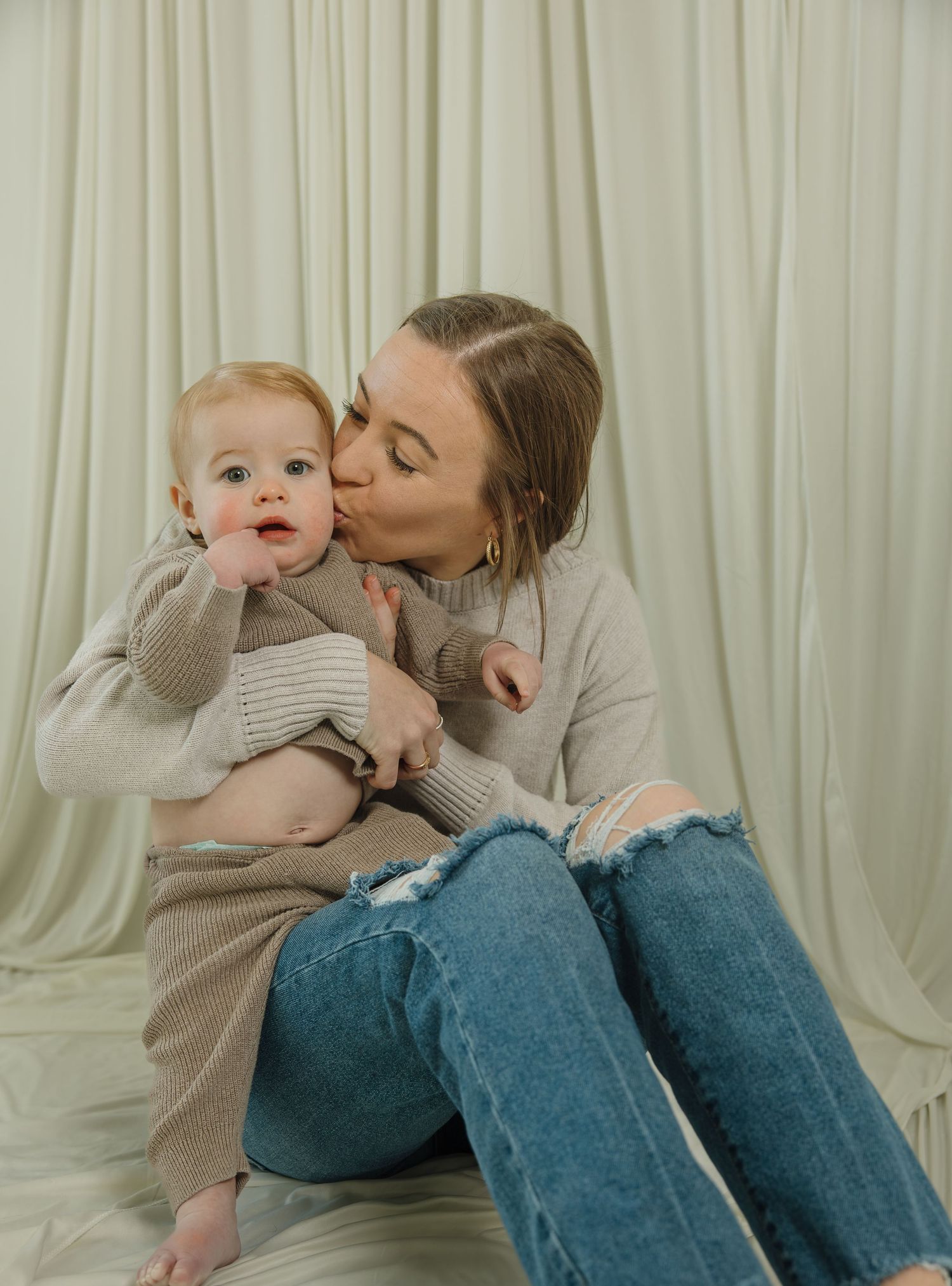 Sweet cuddles and kisses shared on a white backdrop in coordinated neutral outfits.