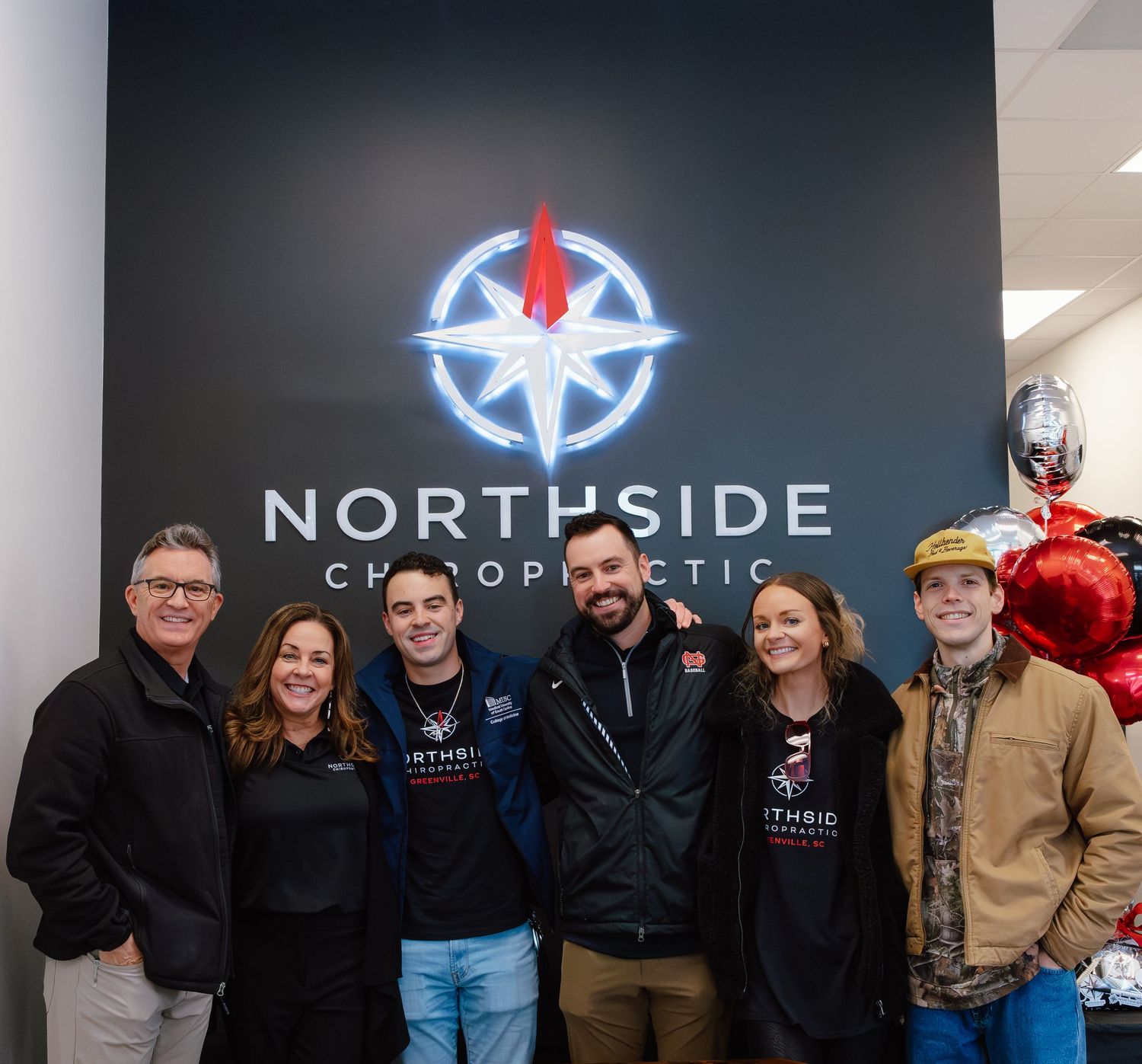 A group of people standing together in front of a Northside Chiropractic office sign with illuminated logo.