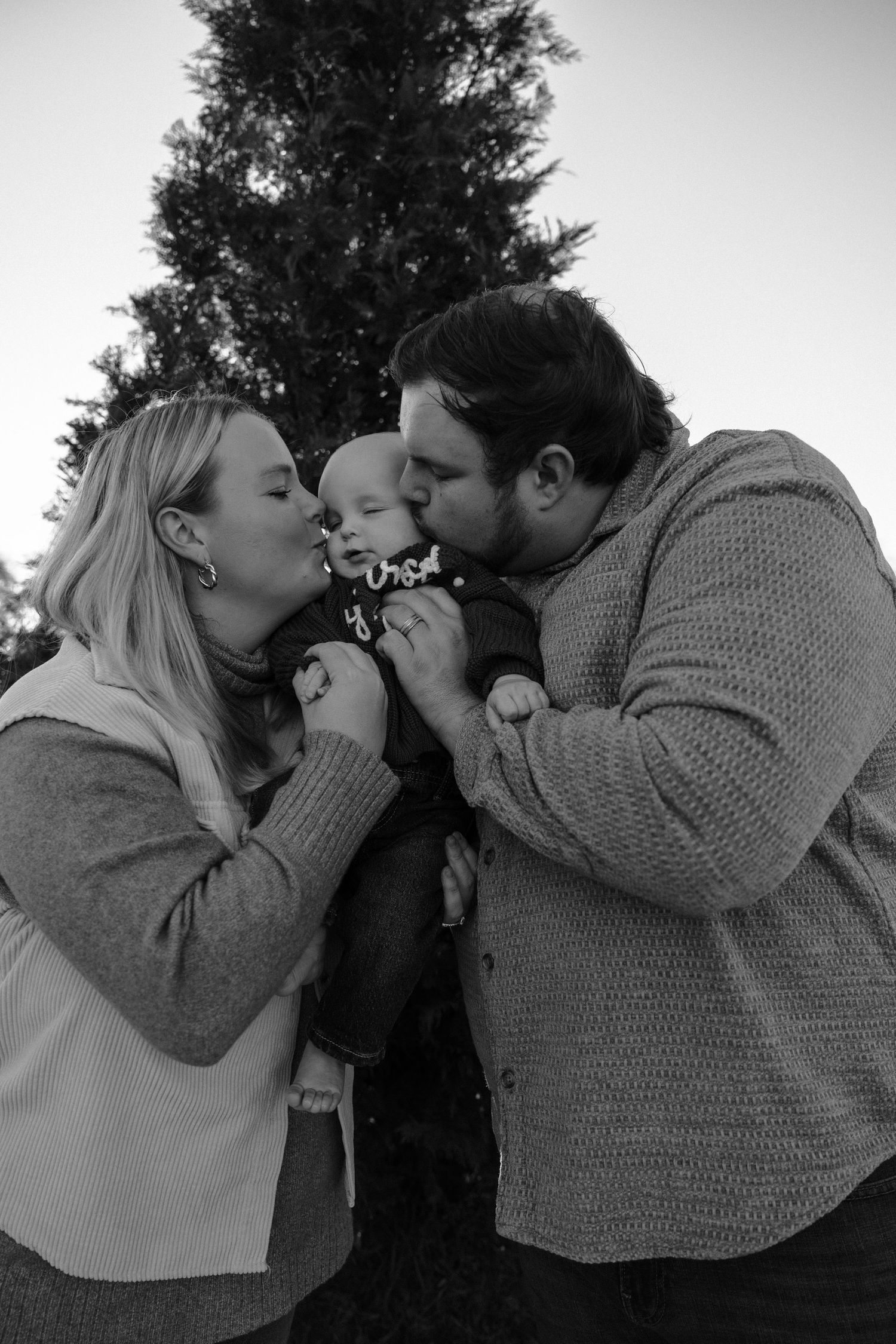 Black and white family portrait sharing intimate moment by Christmas tree.