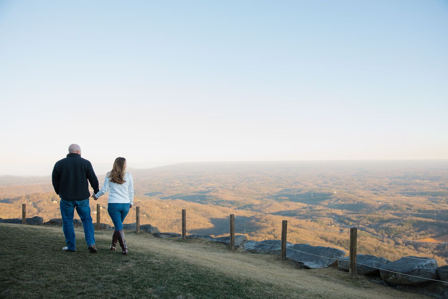 A couple sits together watching the sunset over rolling hills and mountains.
