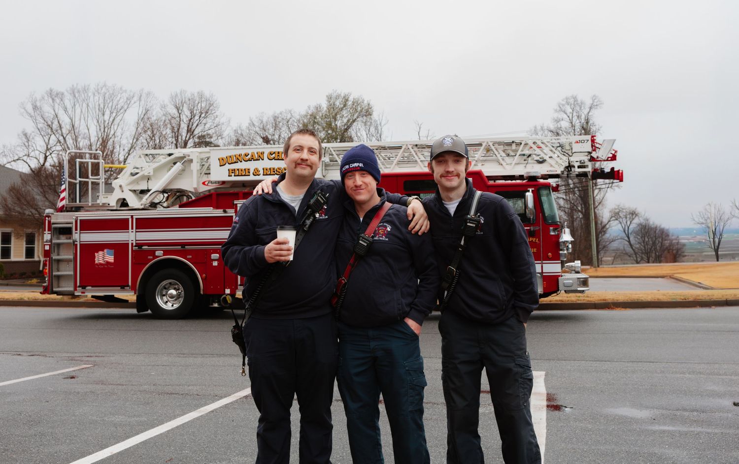 Group of people gathered outside with fire trucks visible in the background during an event.