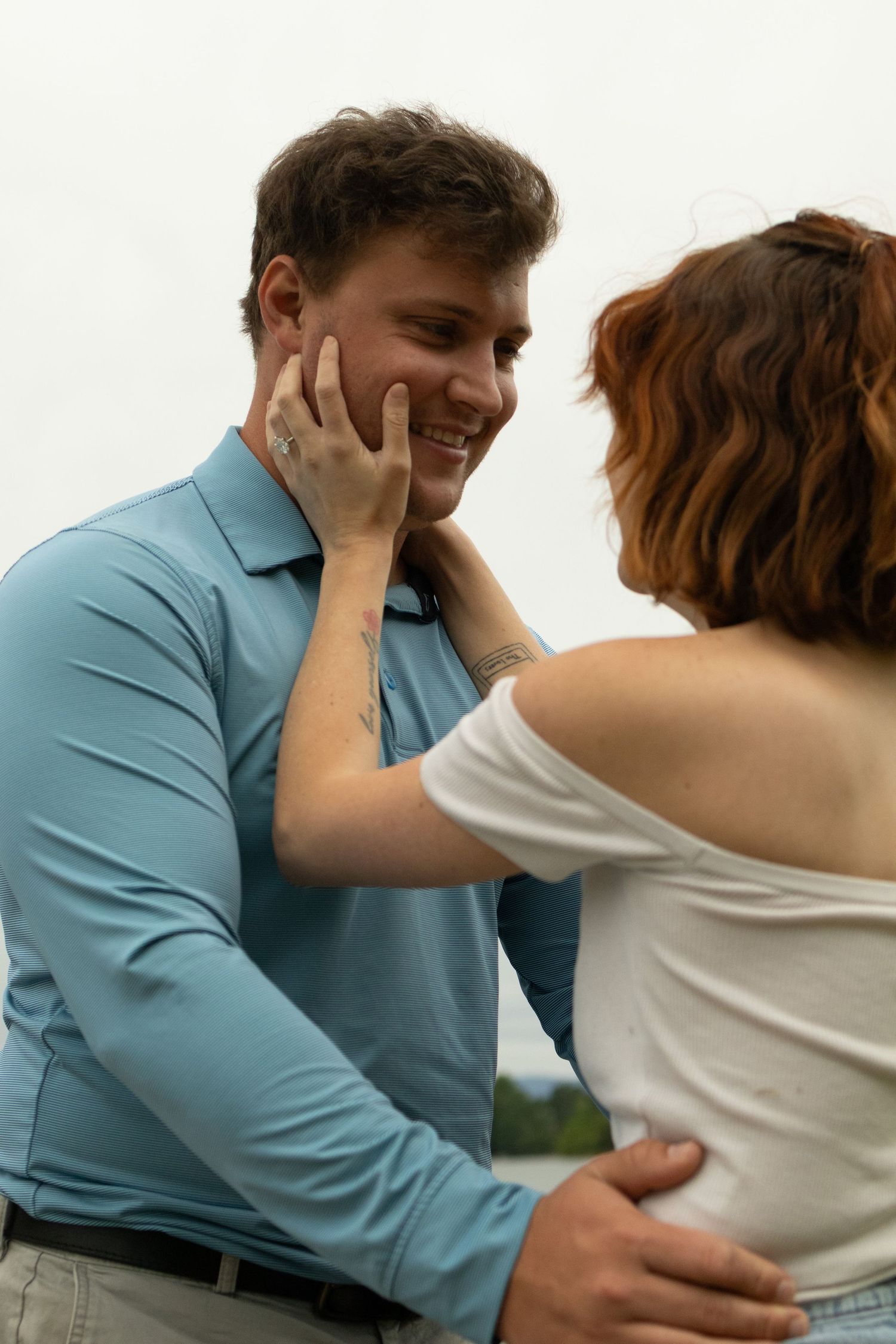 A couple embraces while wearing casual clothes against a white background.