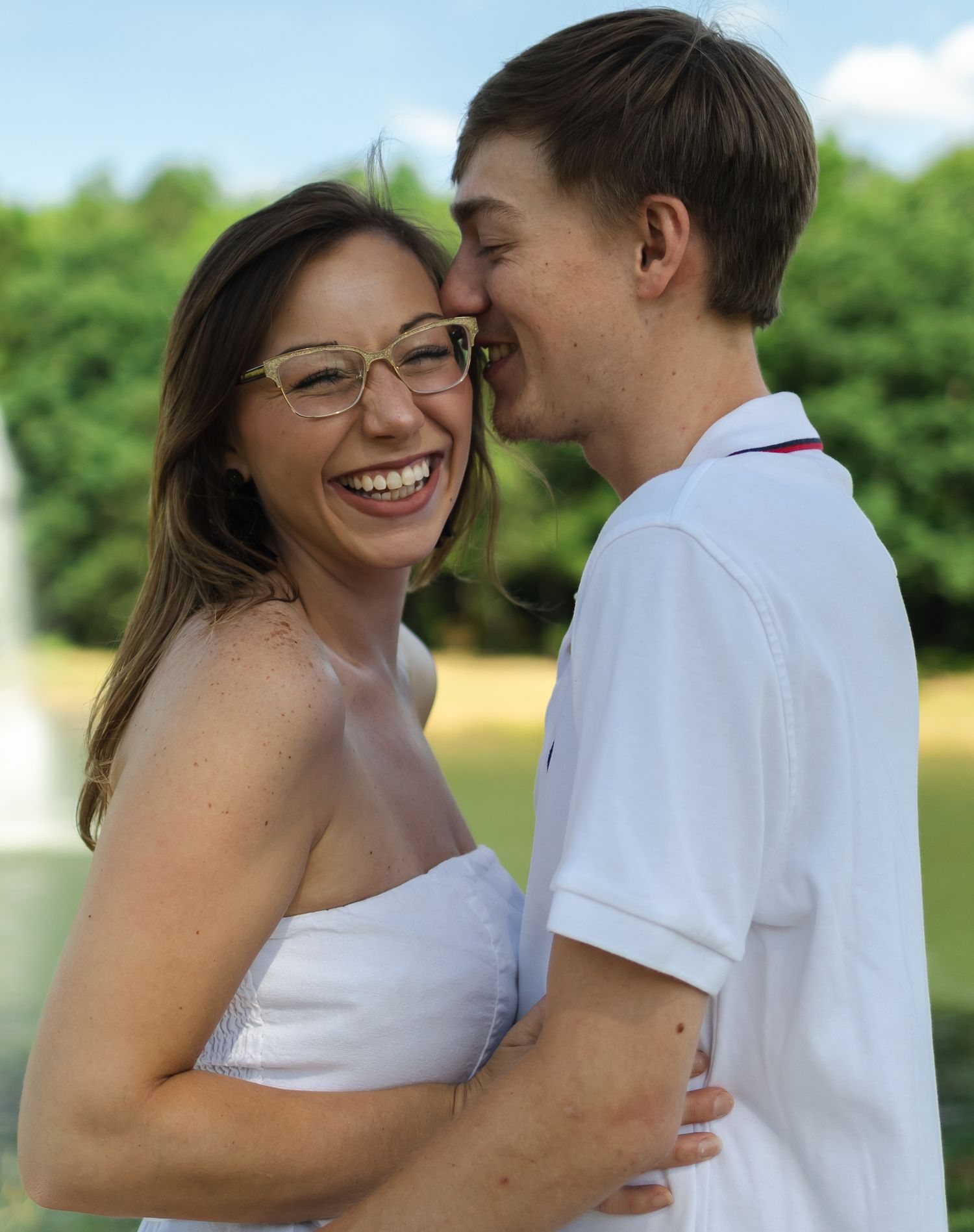 Couple embracing and laughing together in sunny outdoor setting.