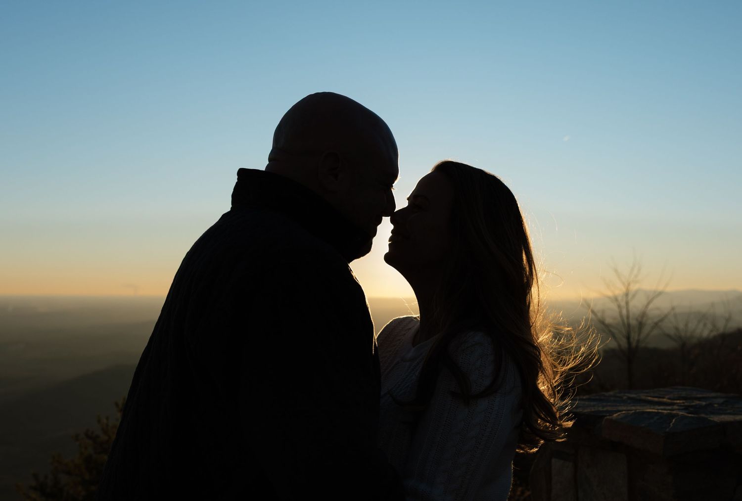Silhouettes of a couple against a dramatic sunset sky on a mountaintop.