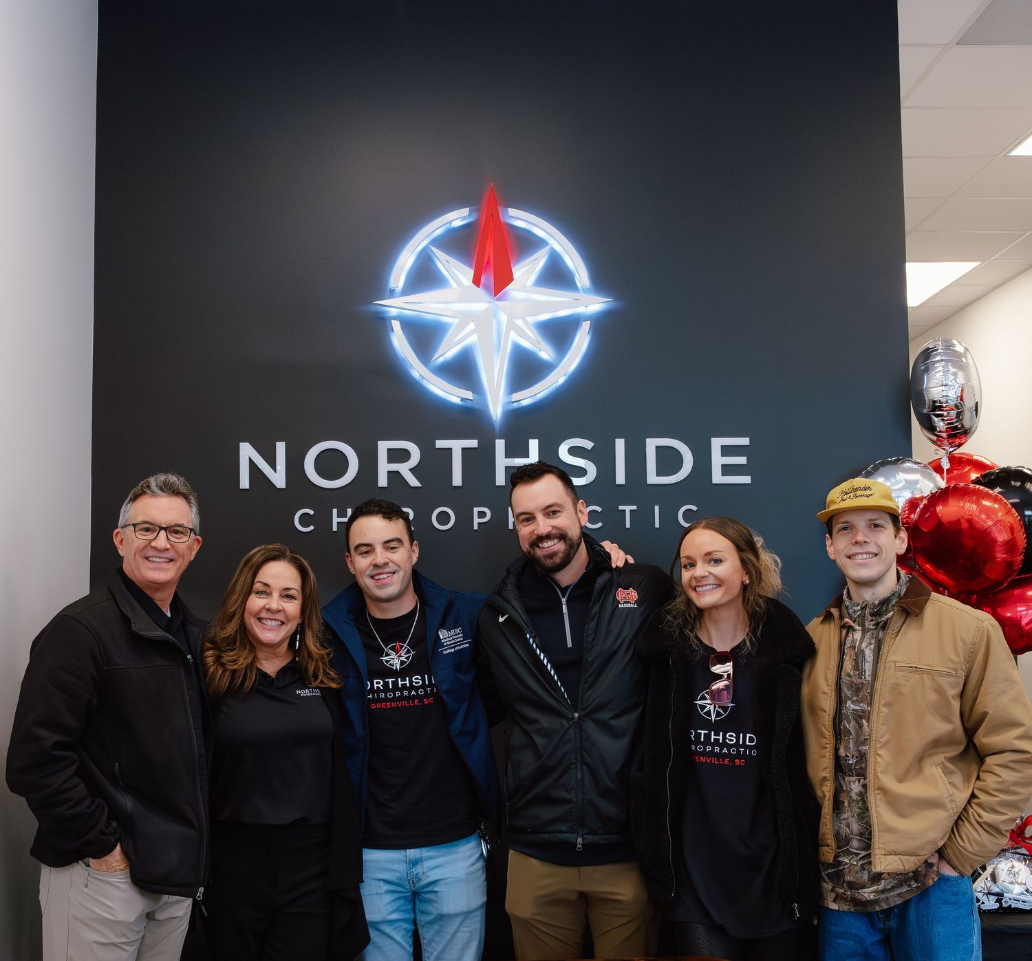 Group photo in front of illuminated Northside Chiropractic business sign on dark wall.