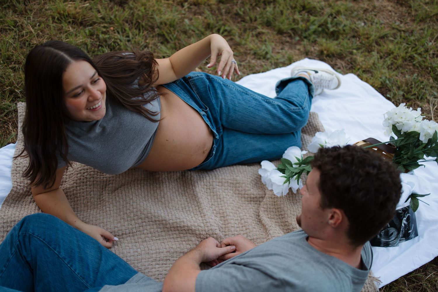 A couple lying on a picnic blanket outdoors having an intimate conversation on the grass.