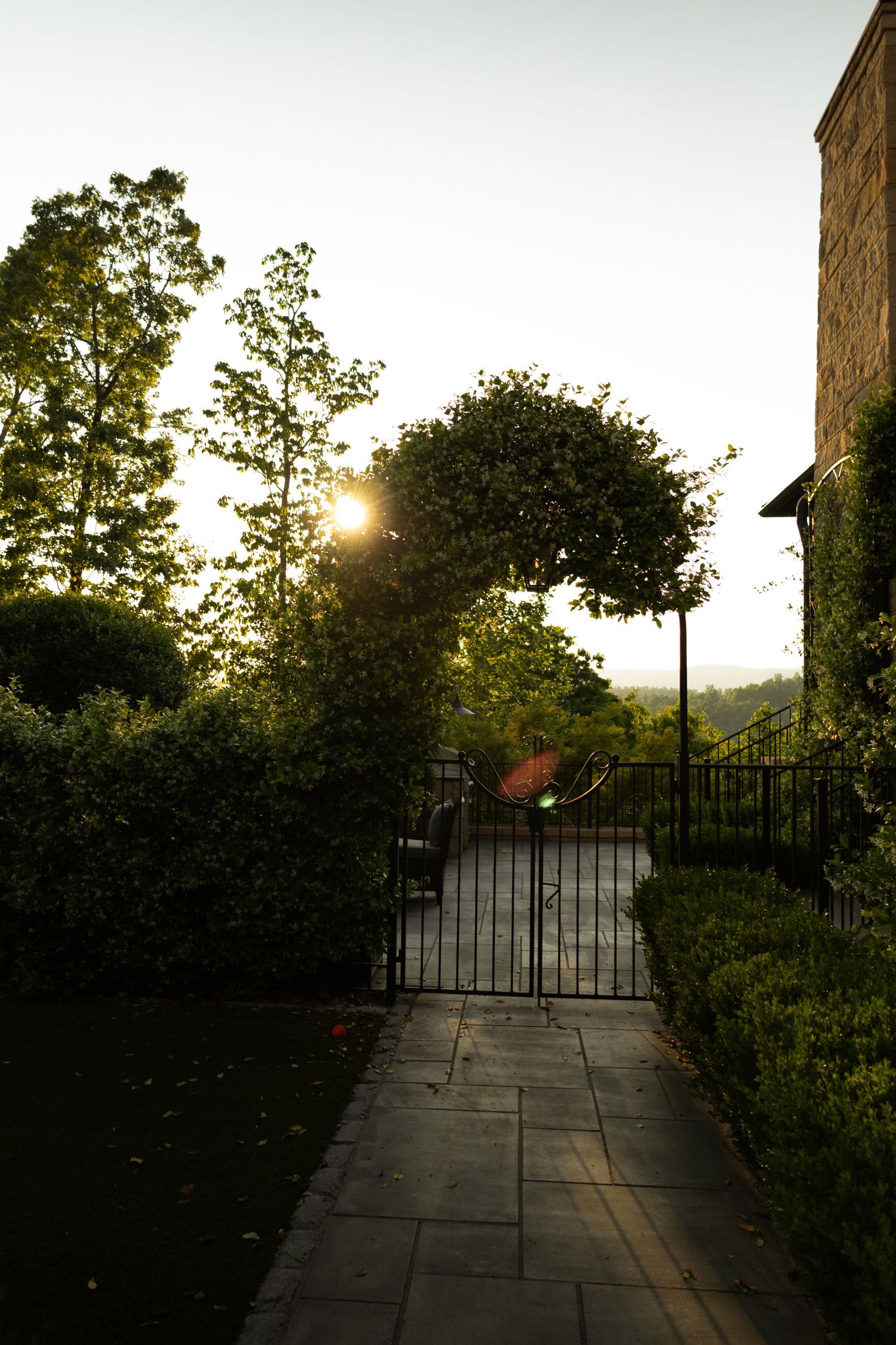 Stone pathway with iron gate leads through garden at sunset.