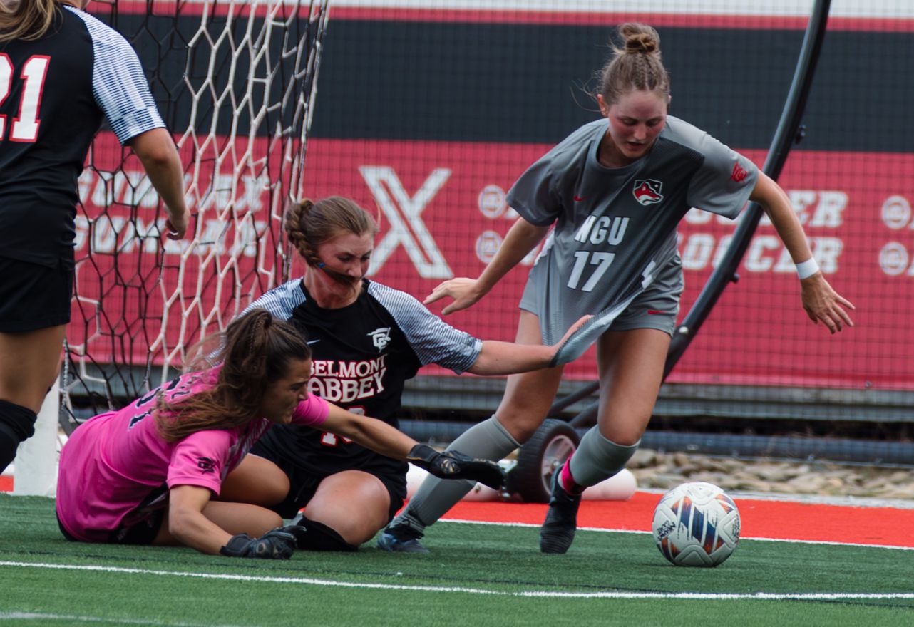Soccer players stretch on a red turf field during practice drills.