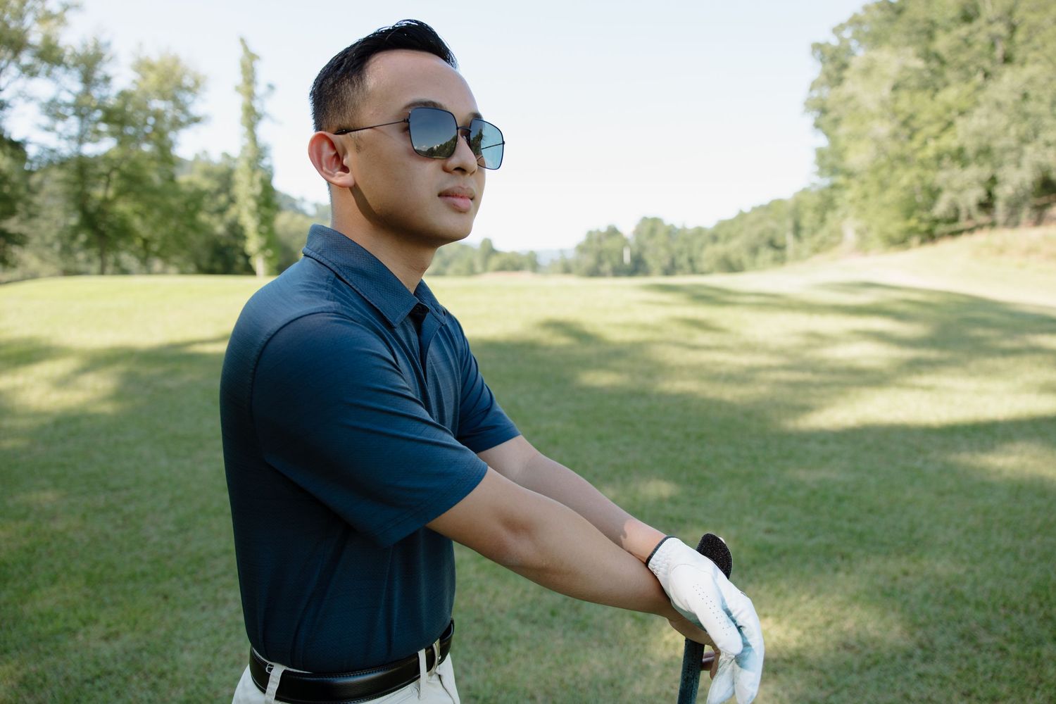 Person in navy polo shirt and khaki shorts posing casually in a sunny outdoor setting.