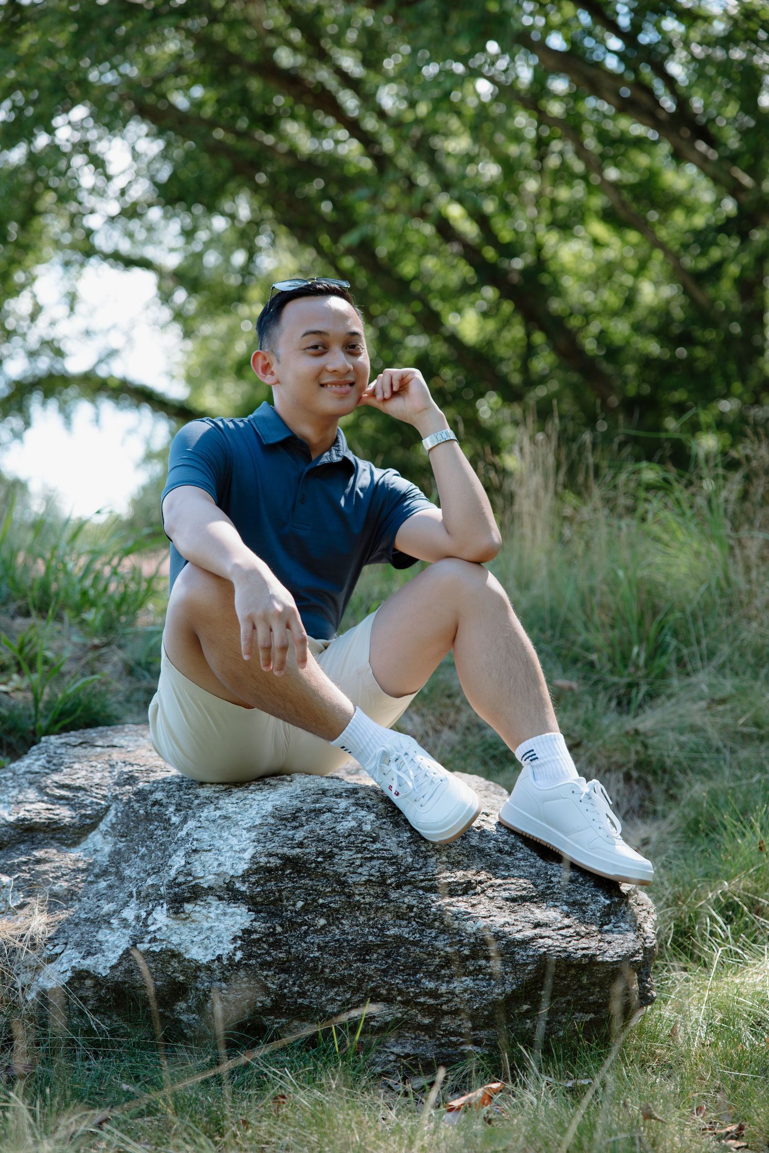 Casual outdoor portrait session showing relaxed poses on a rocky surface surrounded by greenery.