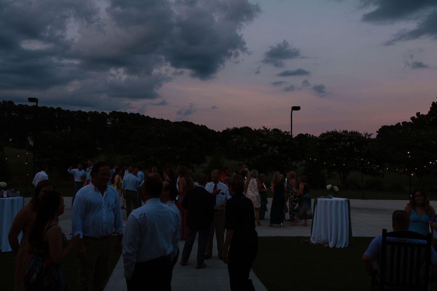 People mingling at an outdoor evening event under dramatic cloudy skies.