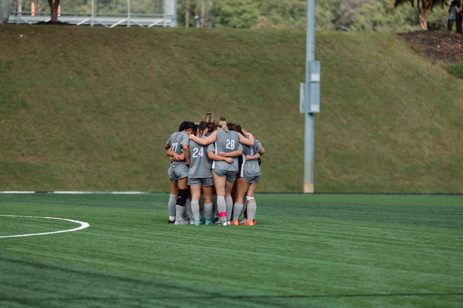Soccer teams resting on field during practice break with goal posts visible.