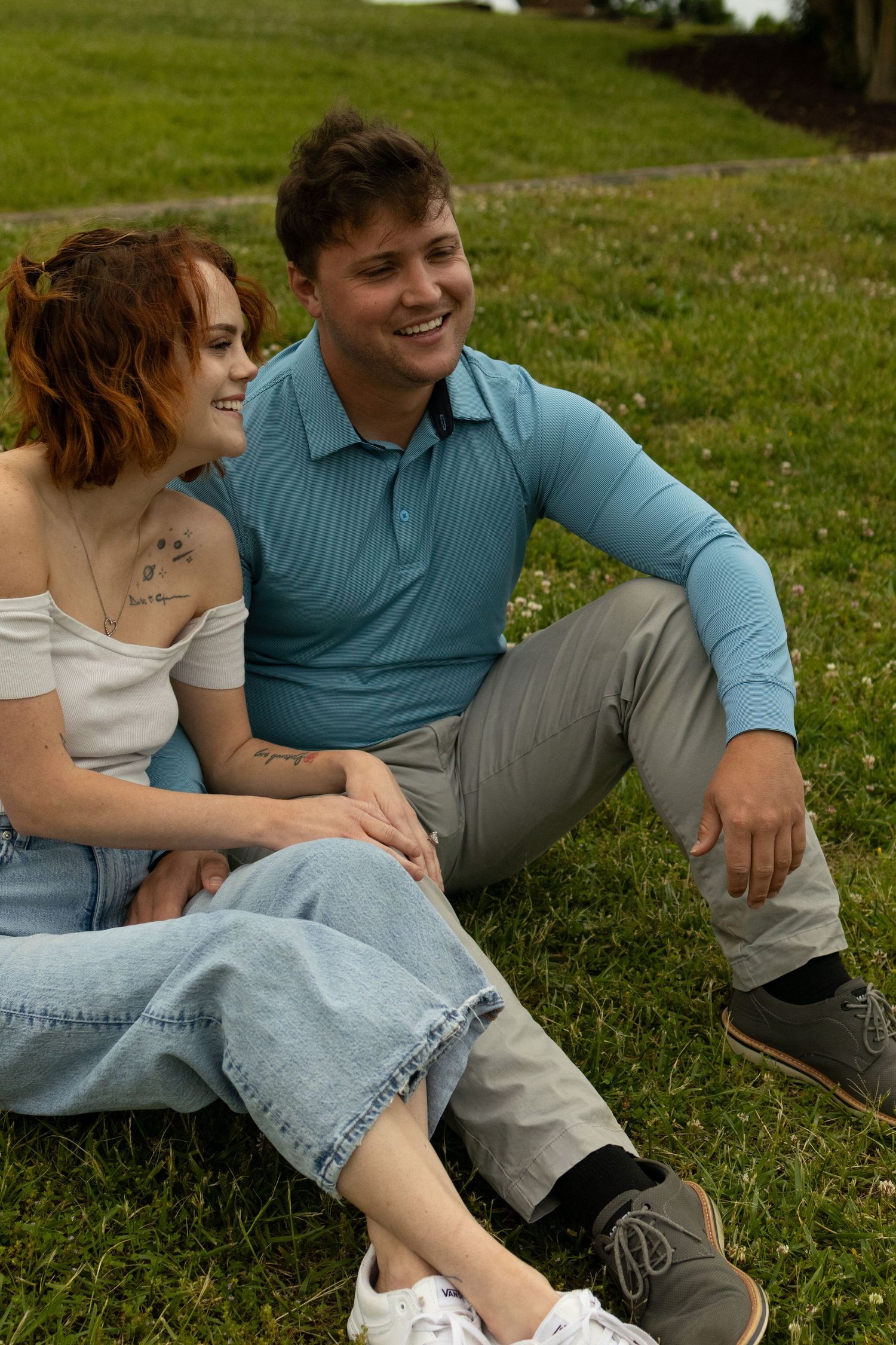 A couple sits together on green grass enjoying a casual outdoor moment in matching teal and white outfits.