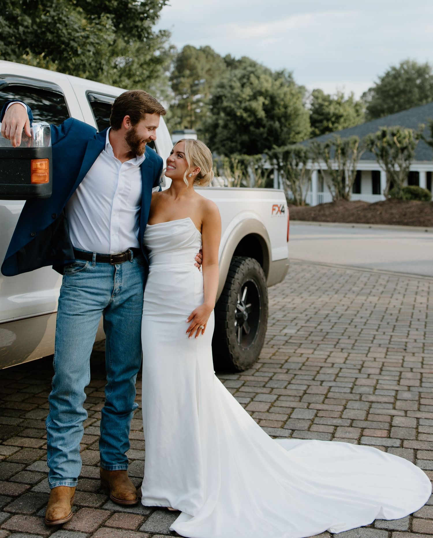 Couple poses against a pickup truck, showing off elegant wedding attire.