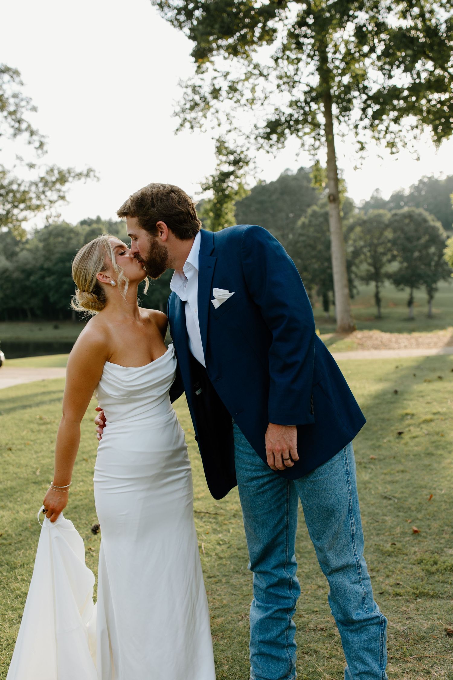 Playful wedding couple poses in casual formal wear on a scenic grassy hill.