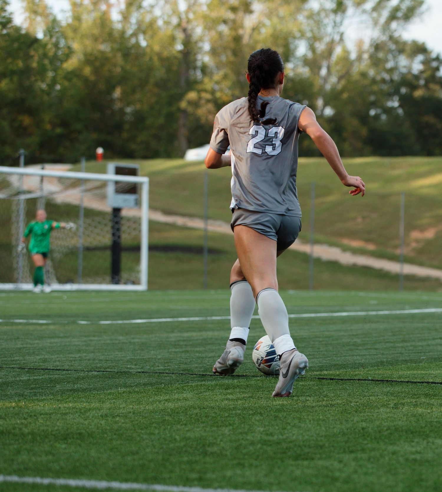 Soccer player dribbles ball across green turf field during soccer game