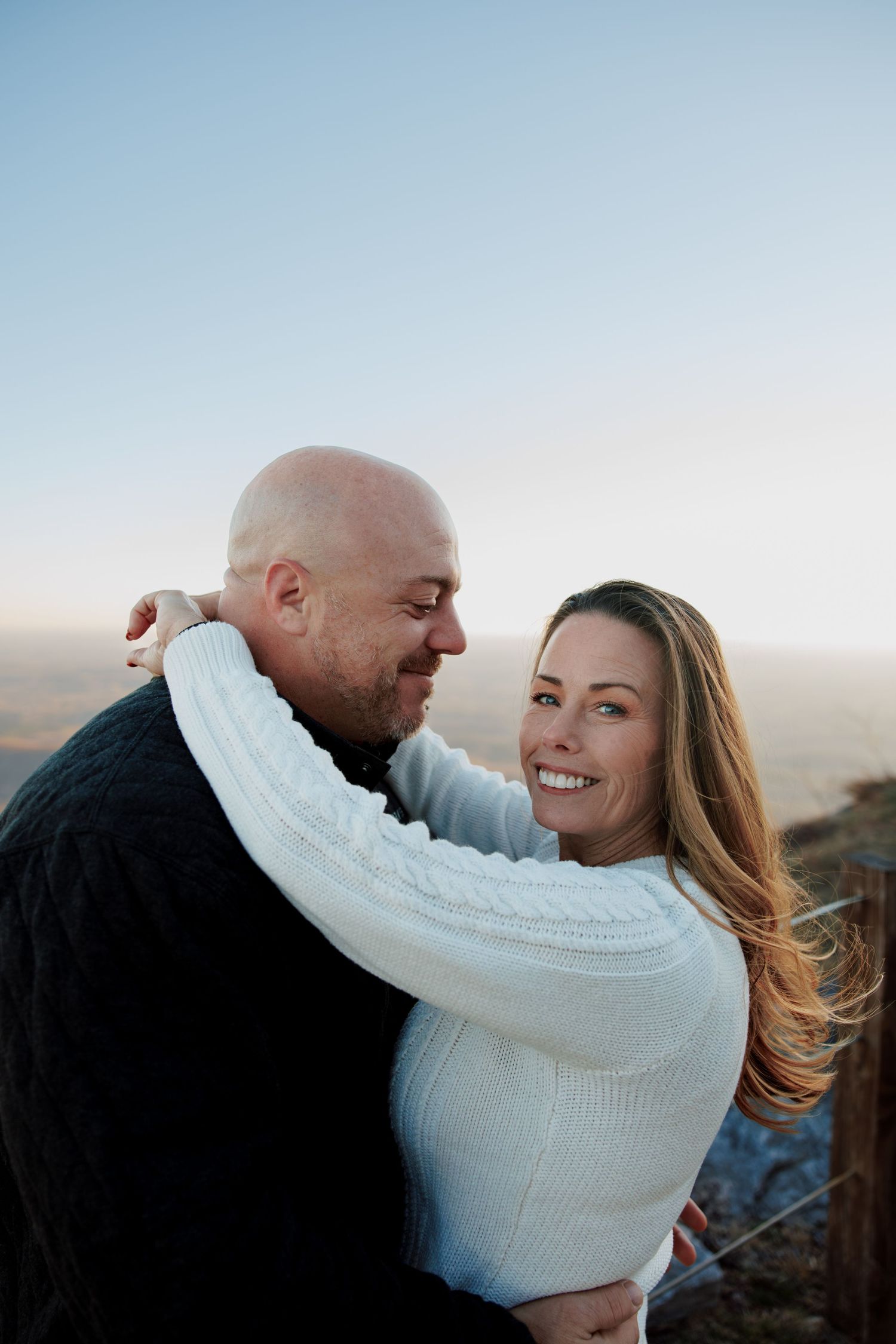 Couple in white sweater and black jacket embrace during outdoor winter photoshoot.