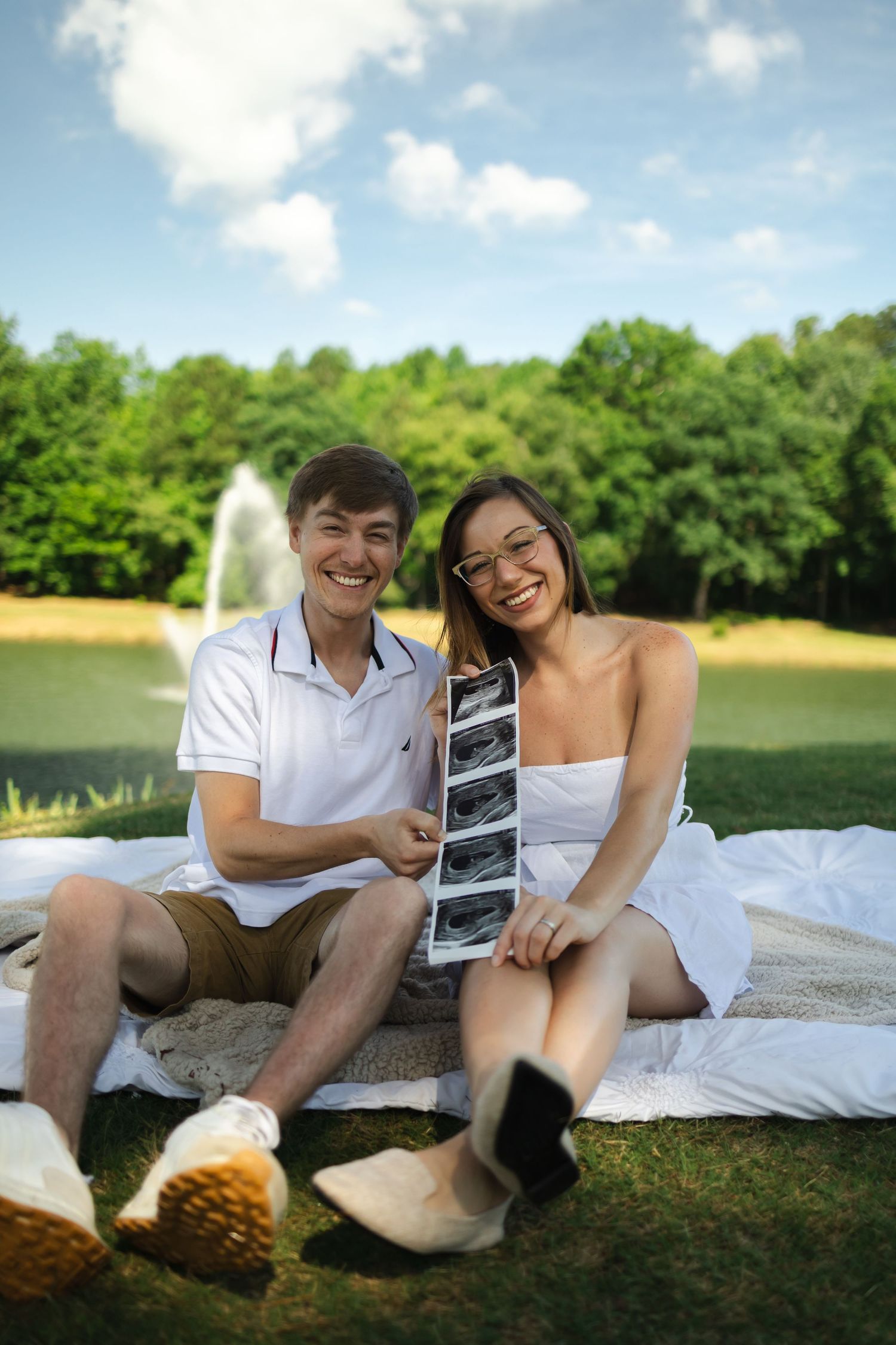 Happy couple sitting on blanket outdoors looking at ultrasound photos.