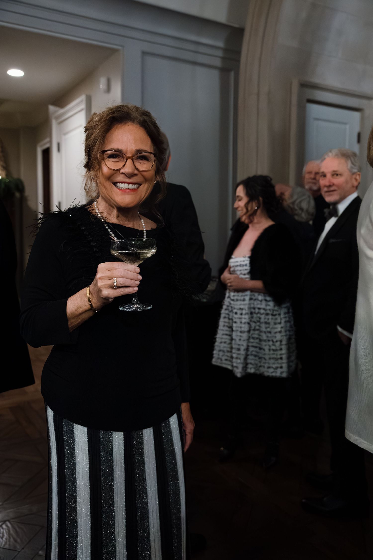 Guests in formal black attire enjoying drinks at an elegant indoor gathering.
