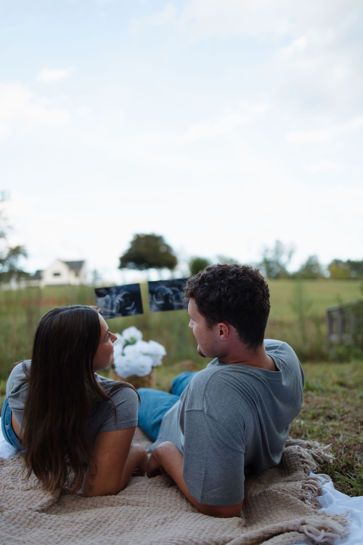 A couple shares an intimate moment while lying on a blanket in a grassy field.